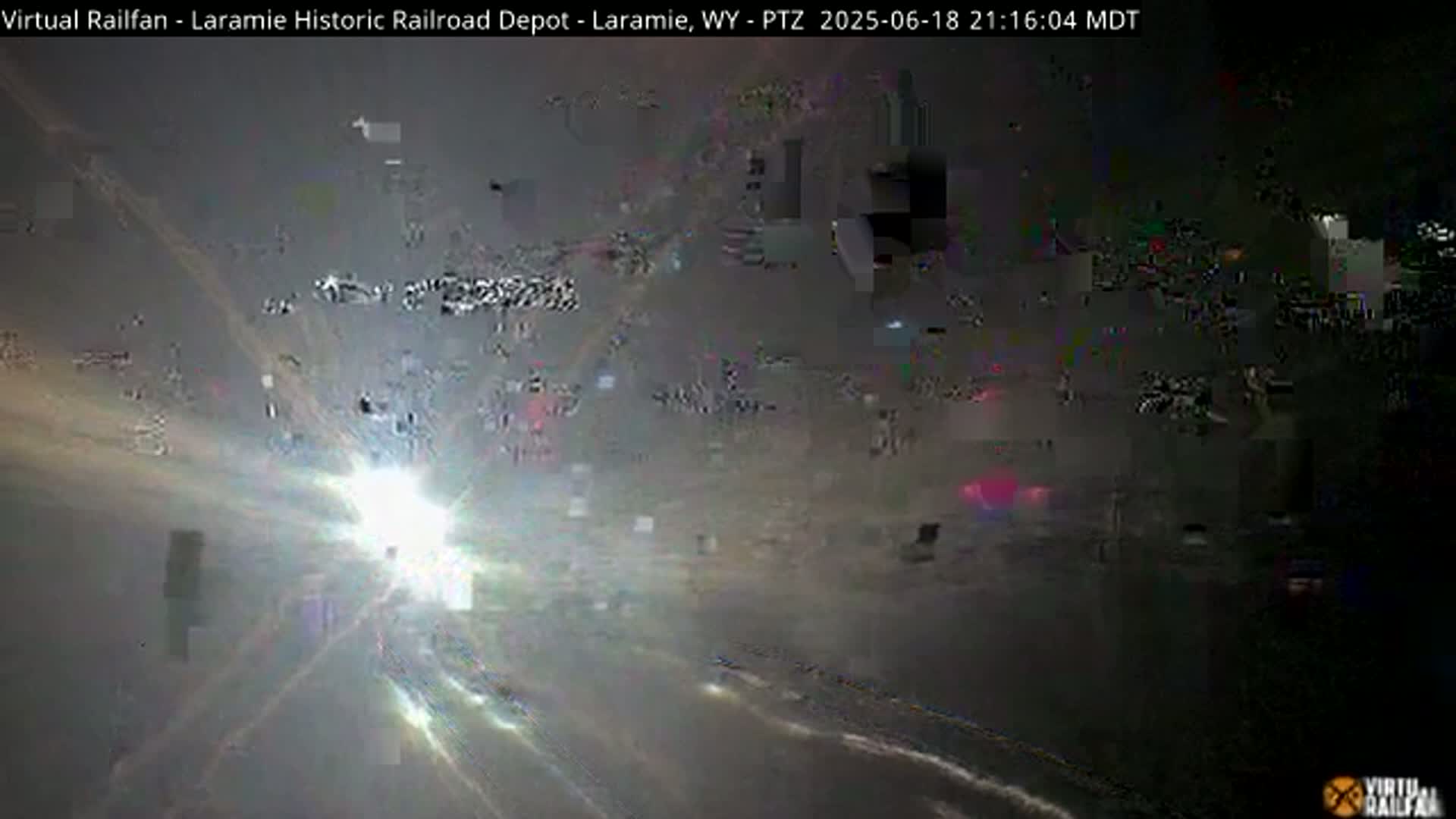 A blurry, sun-streaked nighttime image shows a mostly obscured scene with faint light sources and what appear to be distant vehicles.