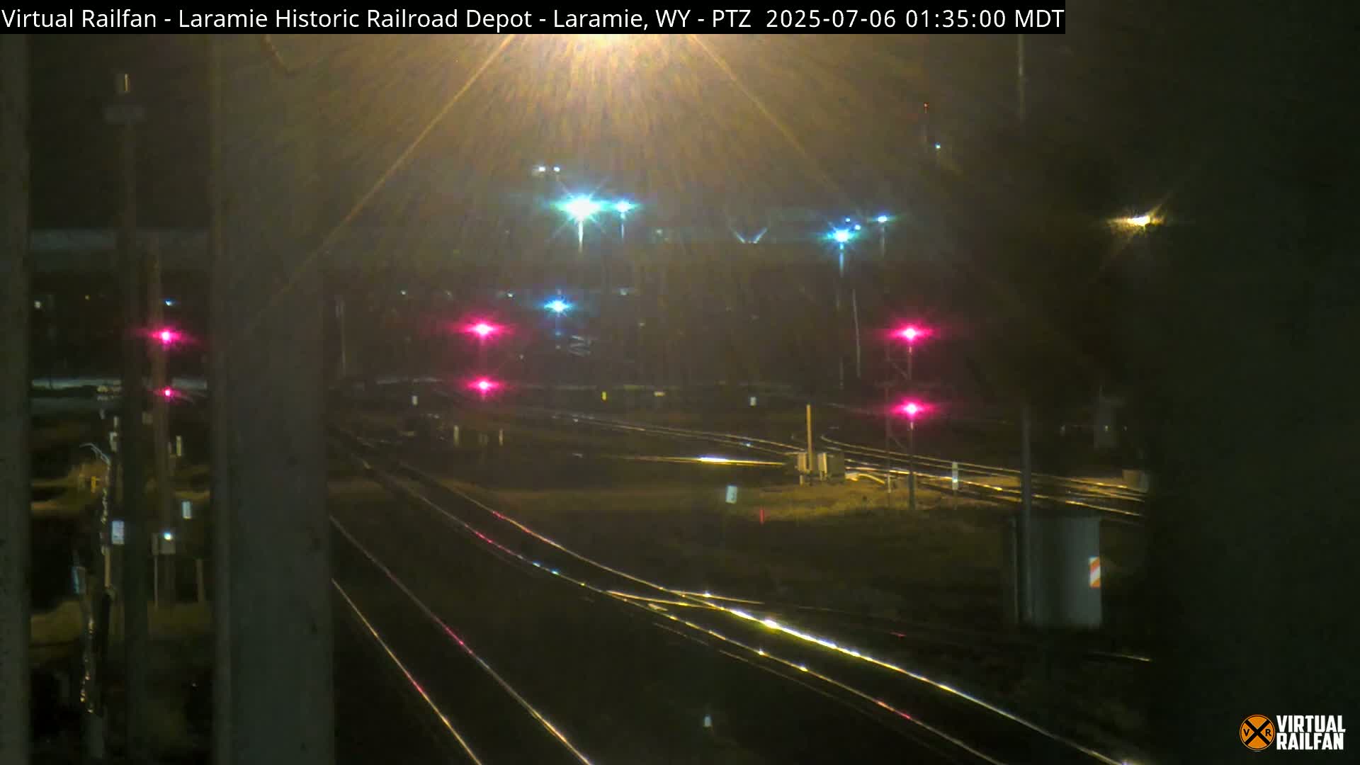 A nighttime view of railroad tracks and signal lights, appearing slightly wet.