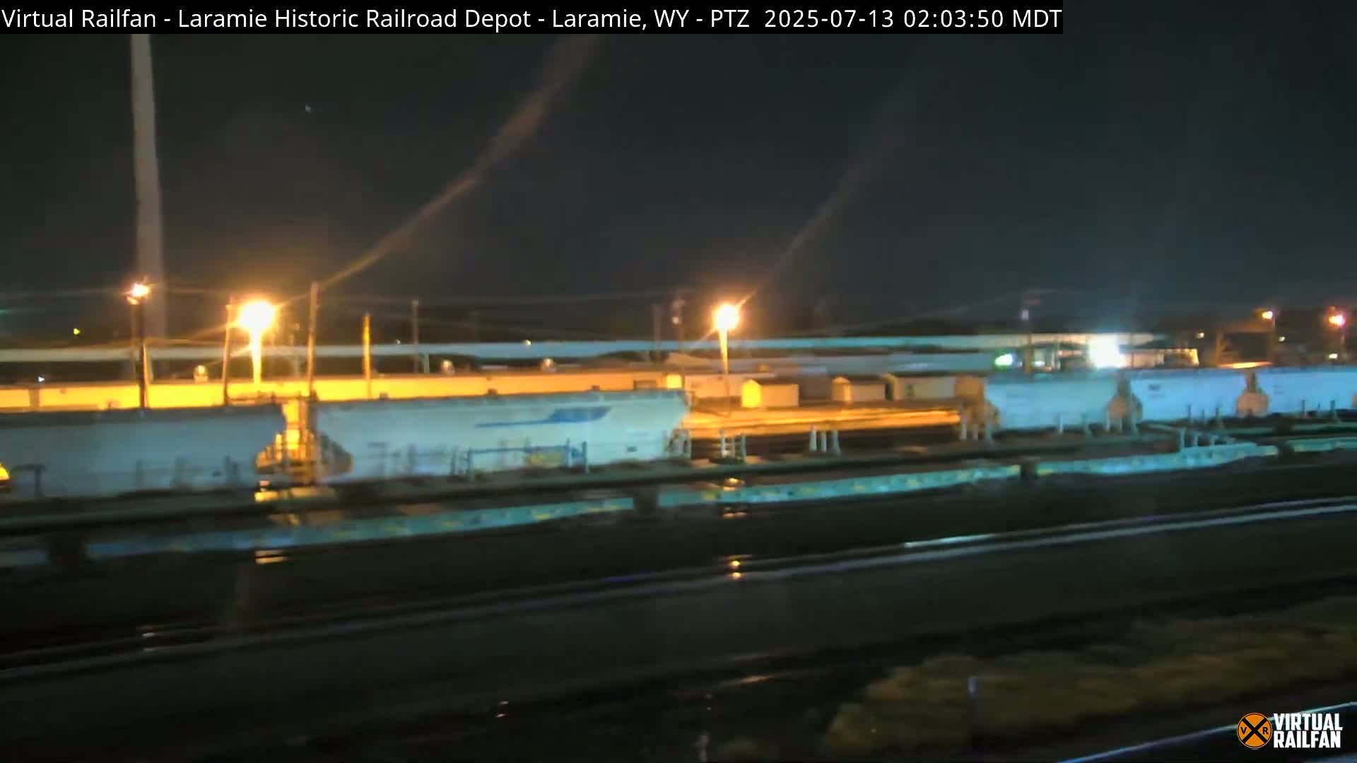 A nighttime view of several long freight train cars parked in a rail yard under a dark sky illuminated by artificial lights.