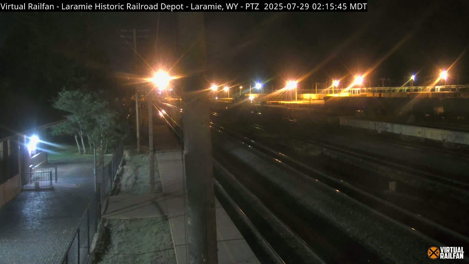 A nighttime view of railroad tracks and a depot, illuminated by streetlights, with clear skies.