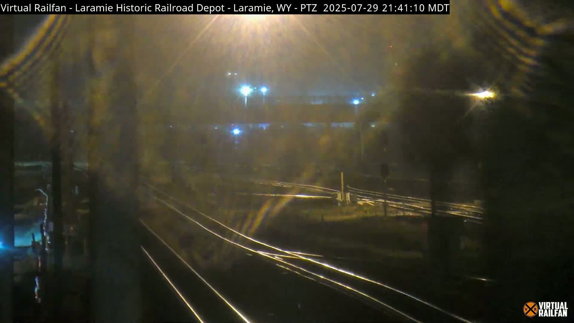 A nighttime view of railroad tracks and a depot, illuminated by streetlights, with clear skies.