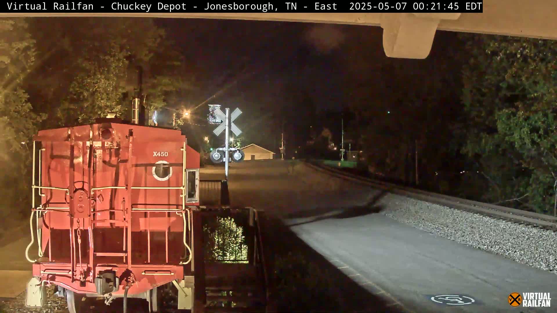 A red train car sits at a nighttime railway crossing, under dark skies.