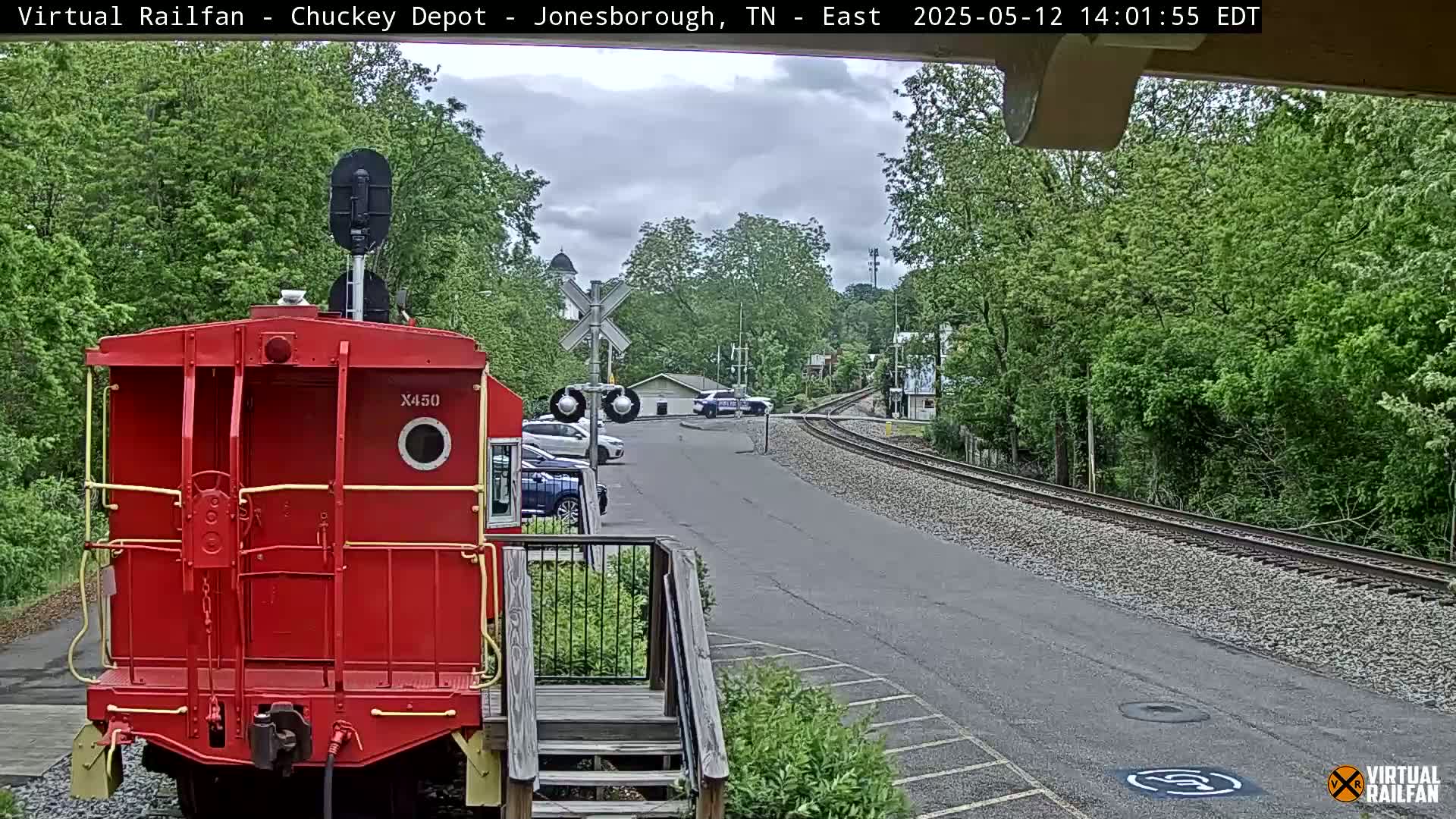 A red railway car is parked at a train depot next to a road, under an overcast sky.