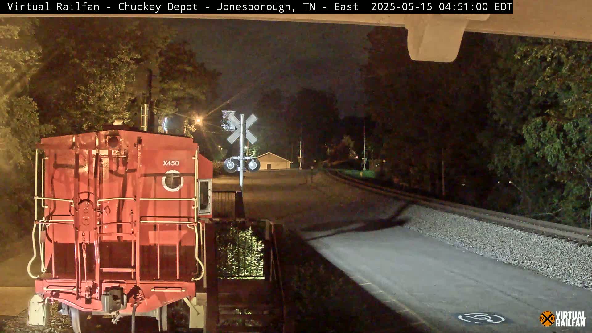 A red train car is stopped at a nighttime railroad crossing near a road.
