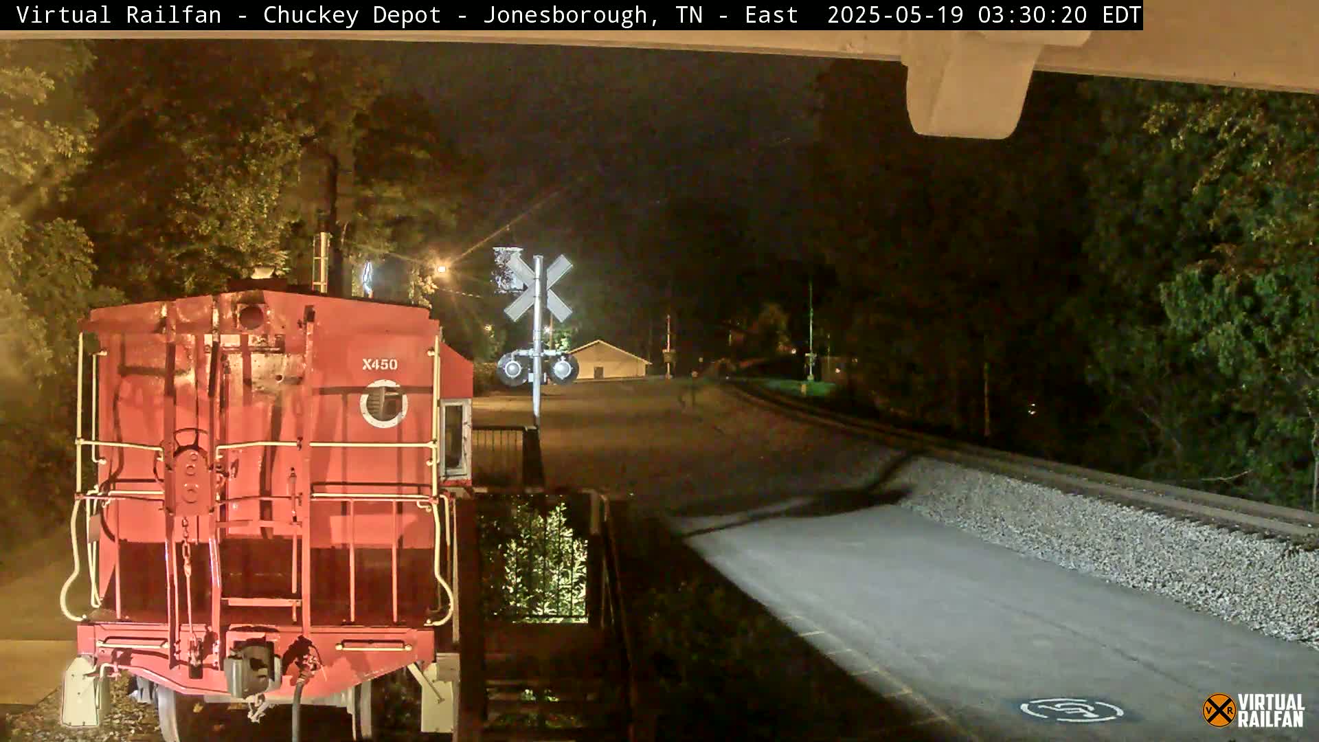 A red railroad engine is stopped at night near a railroad crossing under a dark sky.