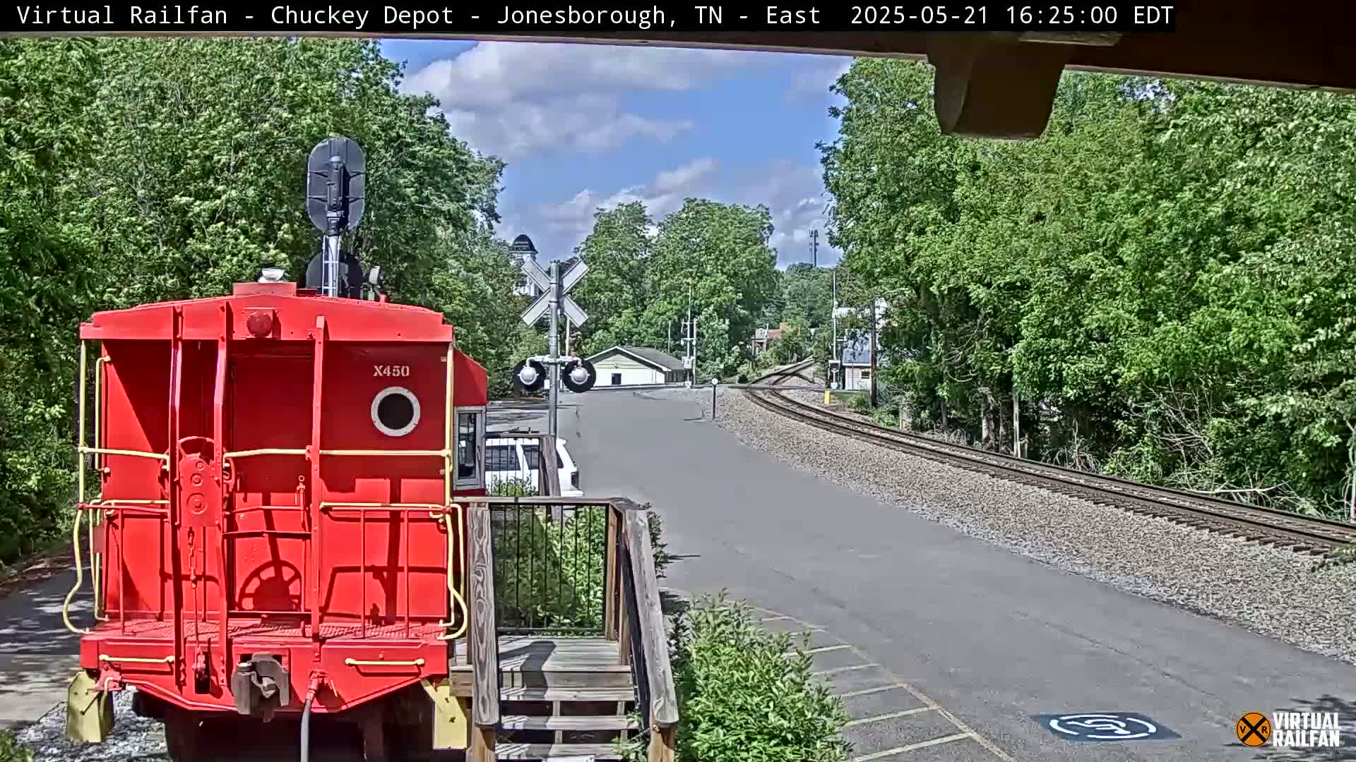 A red railroad car sits in front of a railway line that curves into a distance under a partly cloudy sky.