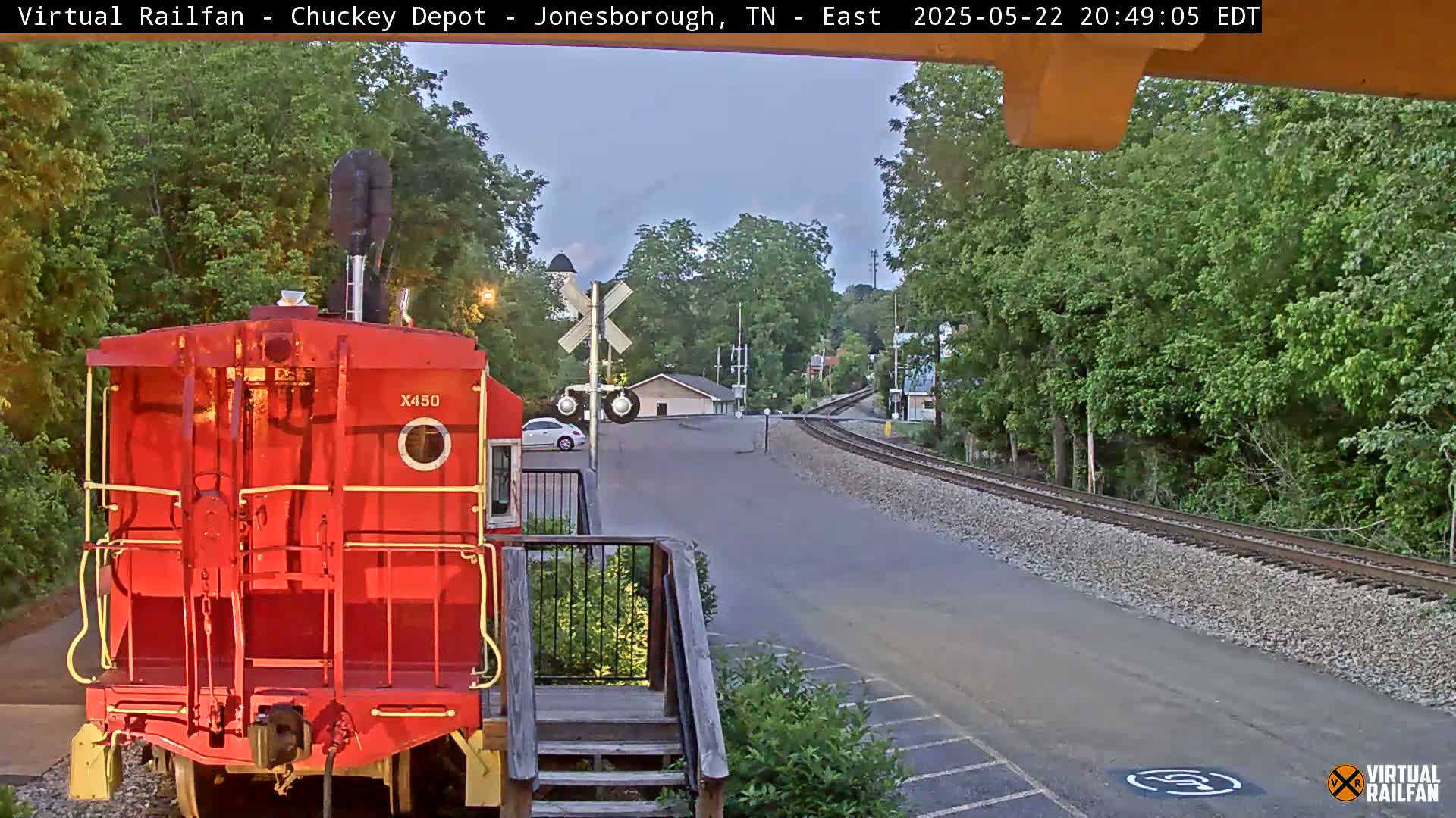 A red train car is parked at a railway crossing near a road under a twilight sky.