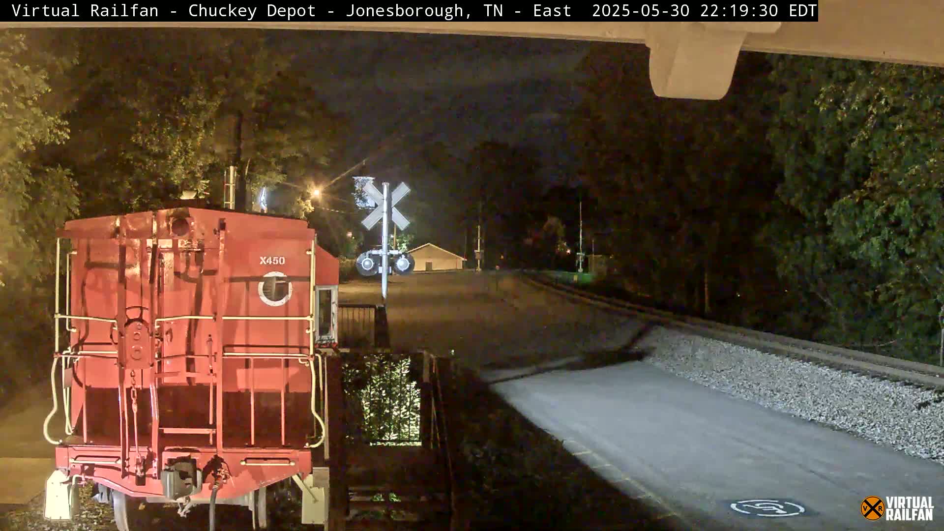 A red train car sits at a nighttime railroad crossing under a dark sky.