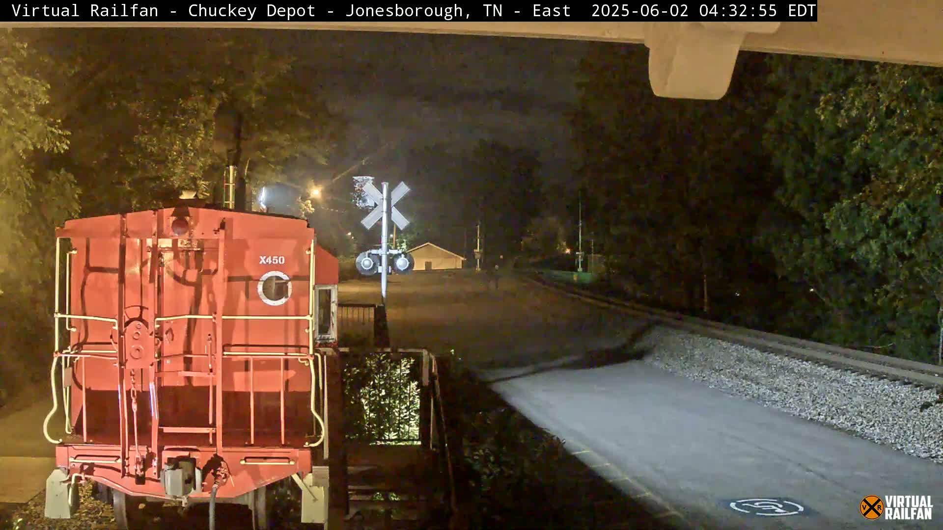 A red train car is parked at night near a railroad crossing, under a dark sky.