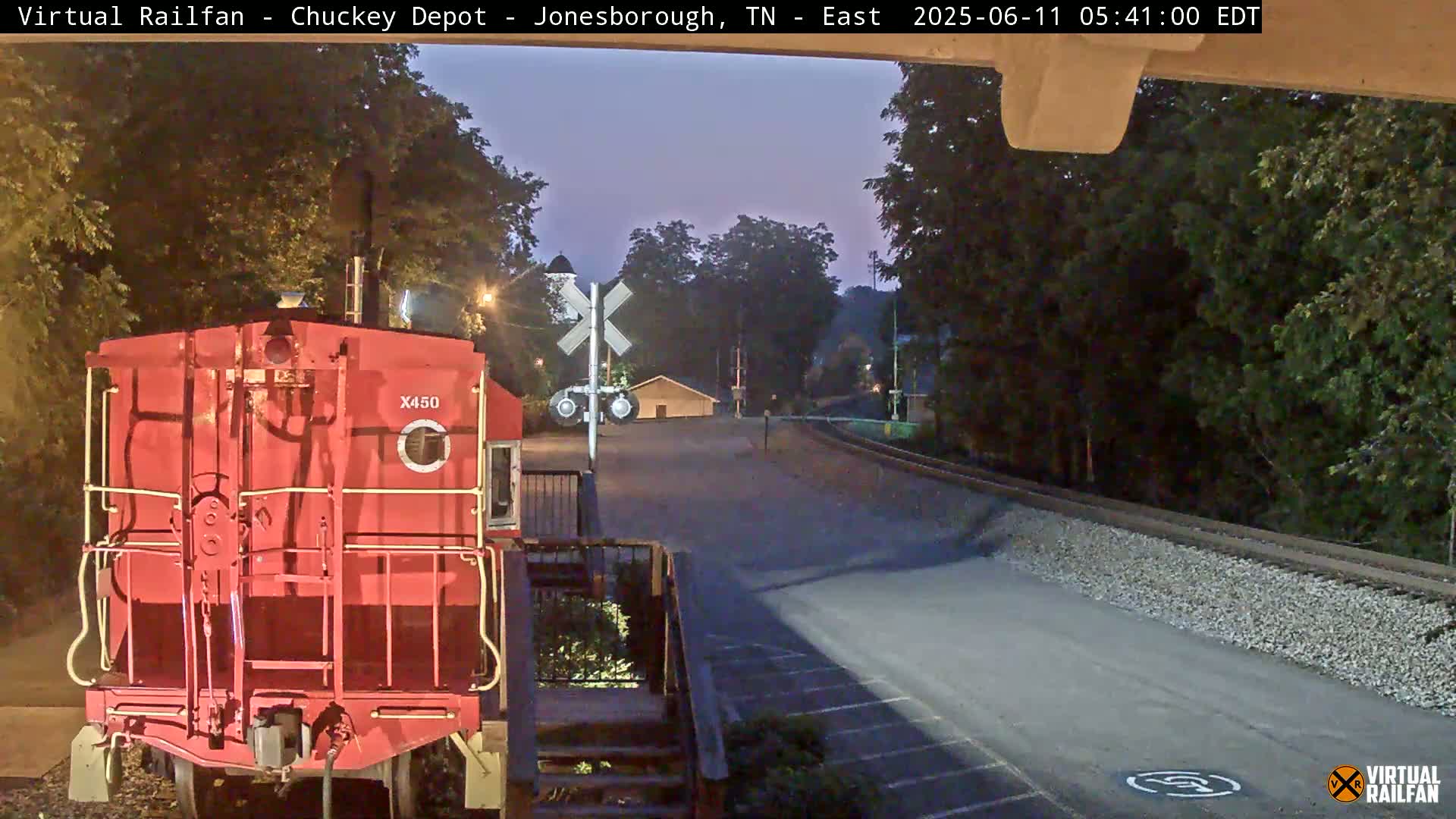 A red train car is parked at a railroad crossing under a twilight sky.