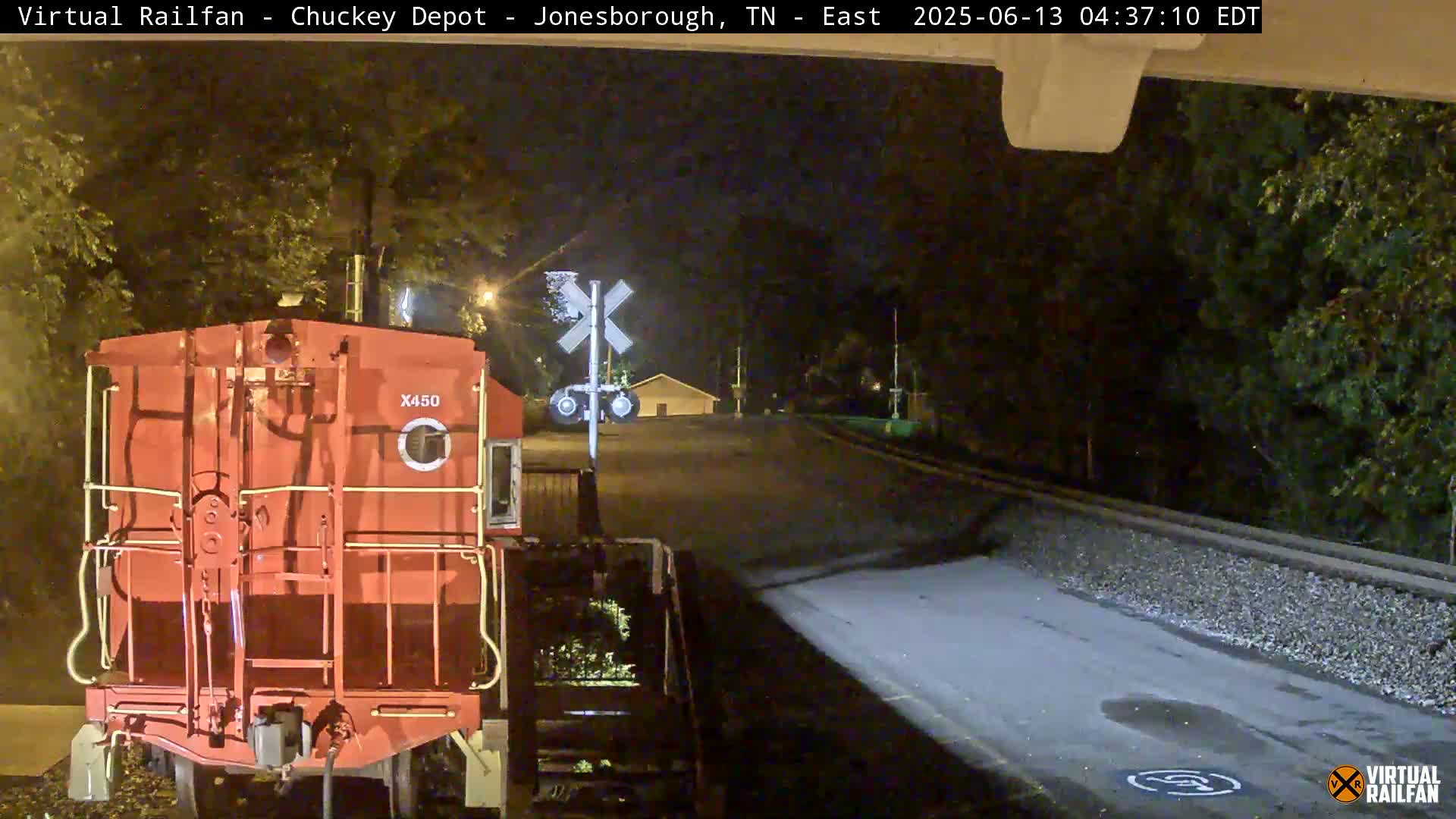 At night, a red train car sits at a railroad crossing near a road.