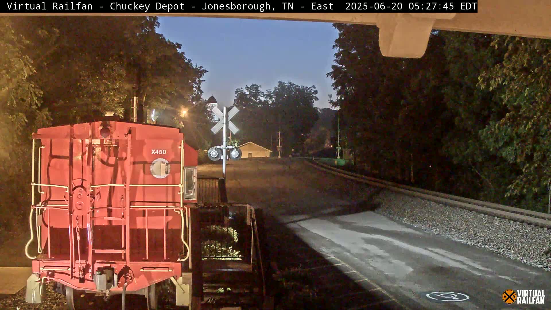 A red train car is parked at a railroad crossing at night under a twilight sky.