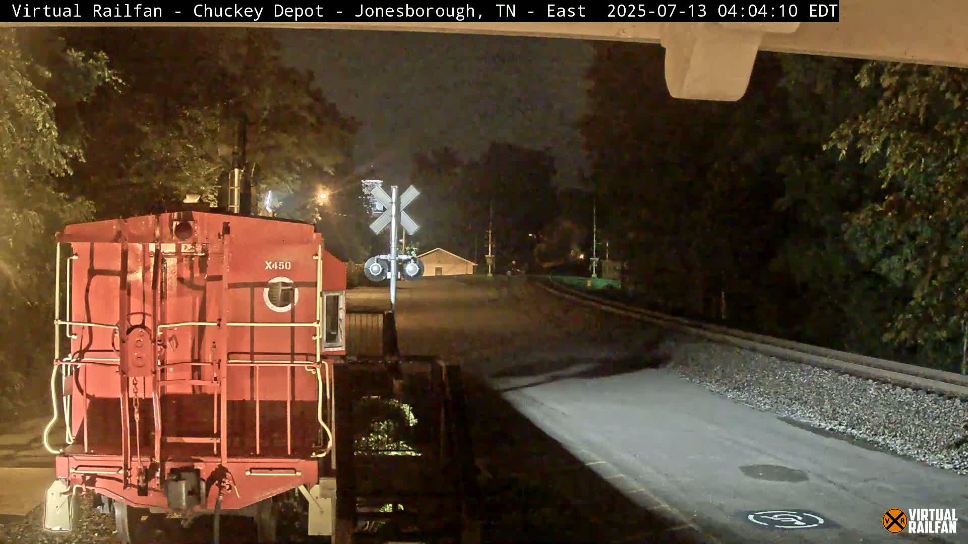 A red railroad car is stopped at a nighttime crossing, under a mostly clear sky.