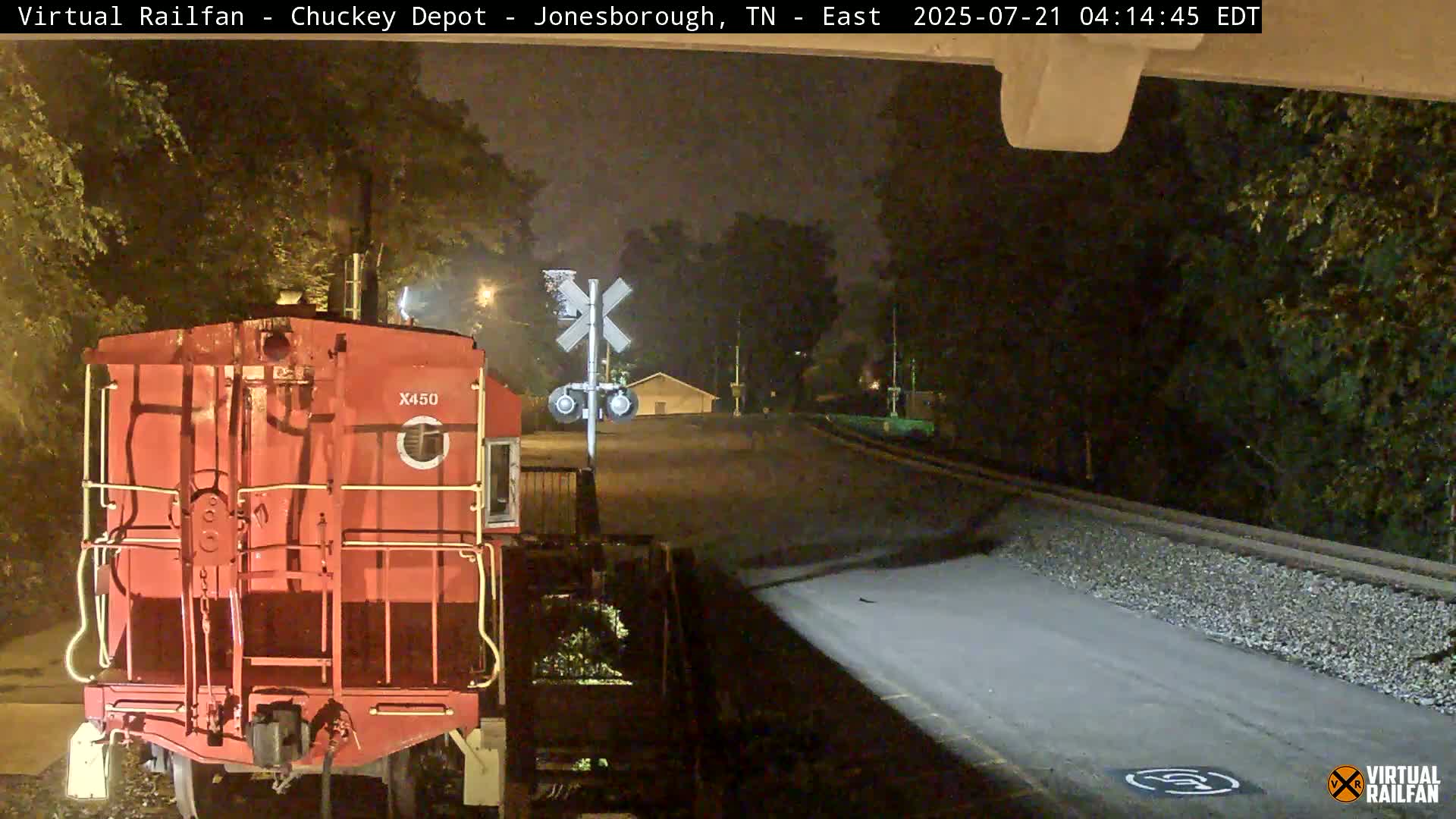 A red train car is stopped at a railroad crossing at night in light rain.