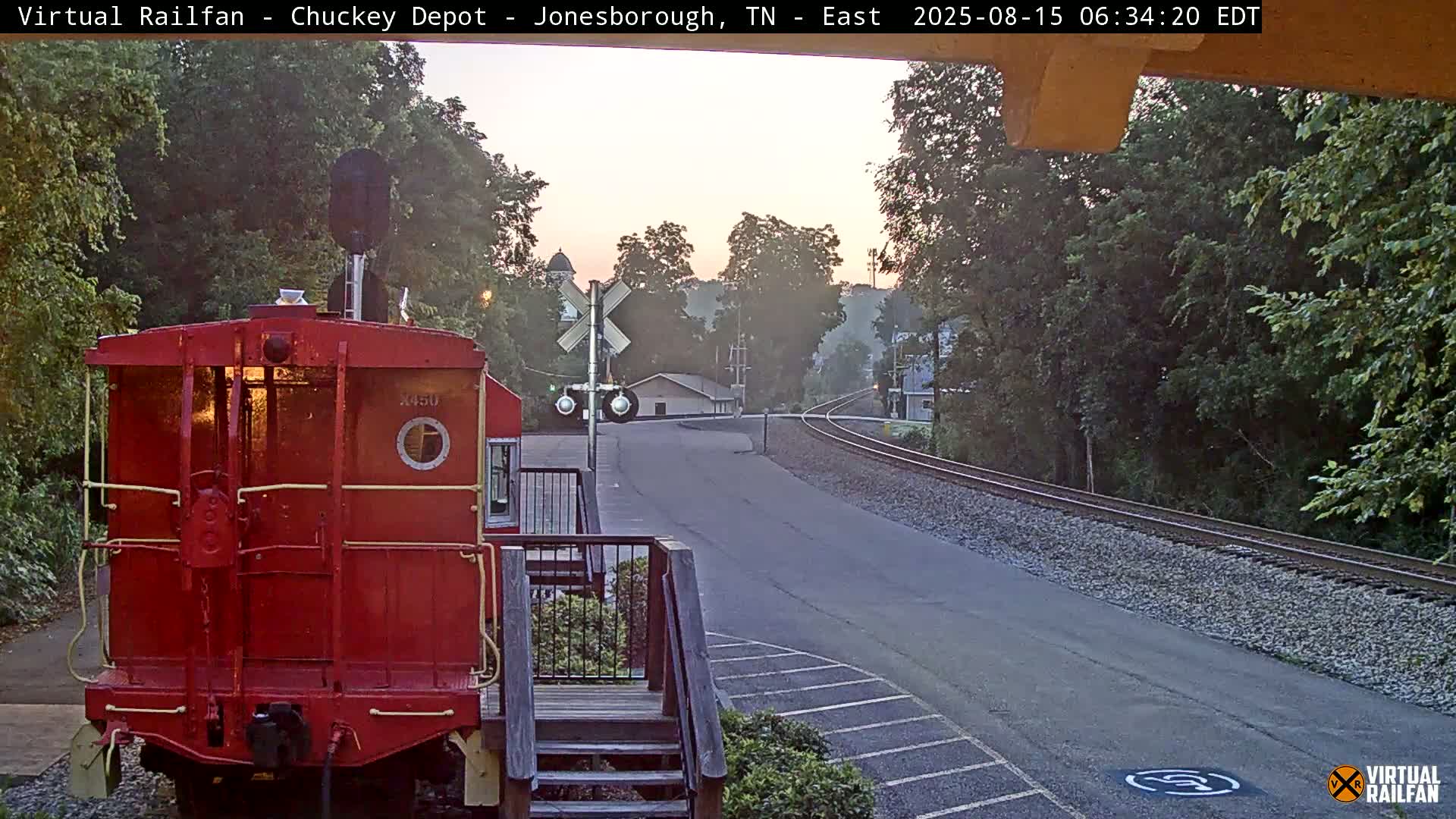 A red railroad car sits at a nighttime railroad crossing under a dark sky.