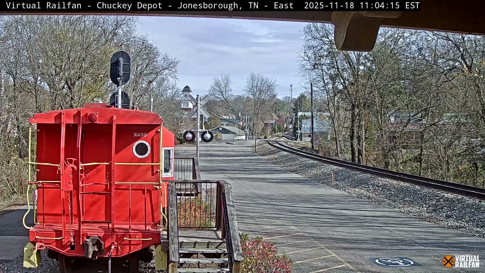 A red railroad car sits at a nighttime railroad crossing under a dark sky.