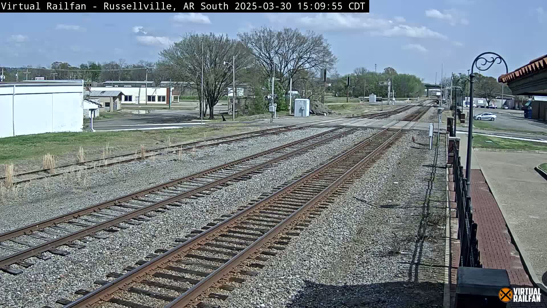Multiple train tracks extend into the distance under a partly cloudy sky, past a small town with buildings and sparse vegetation.