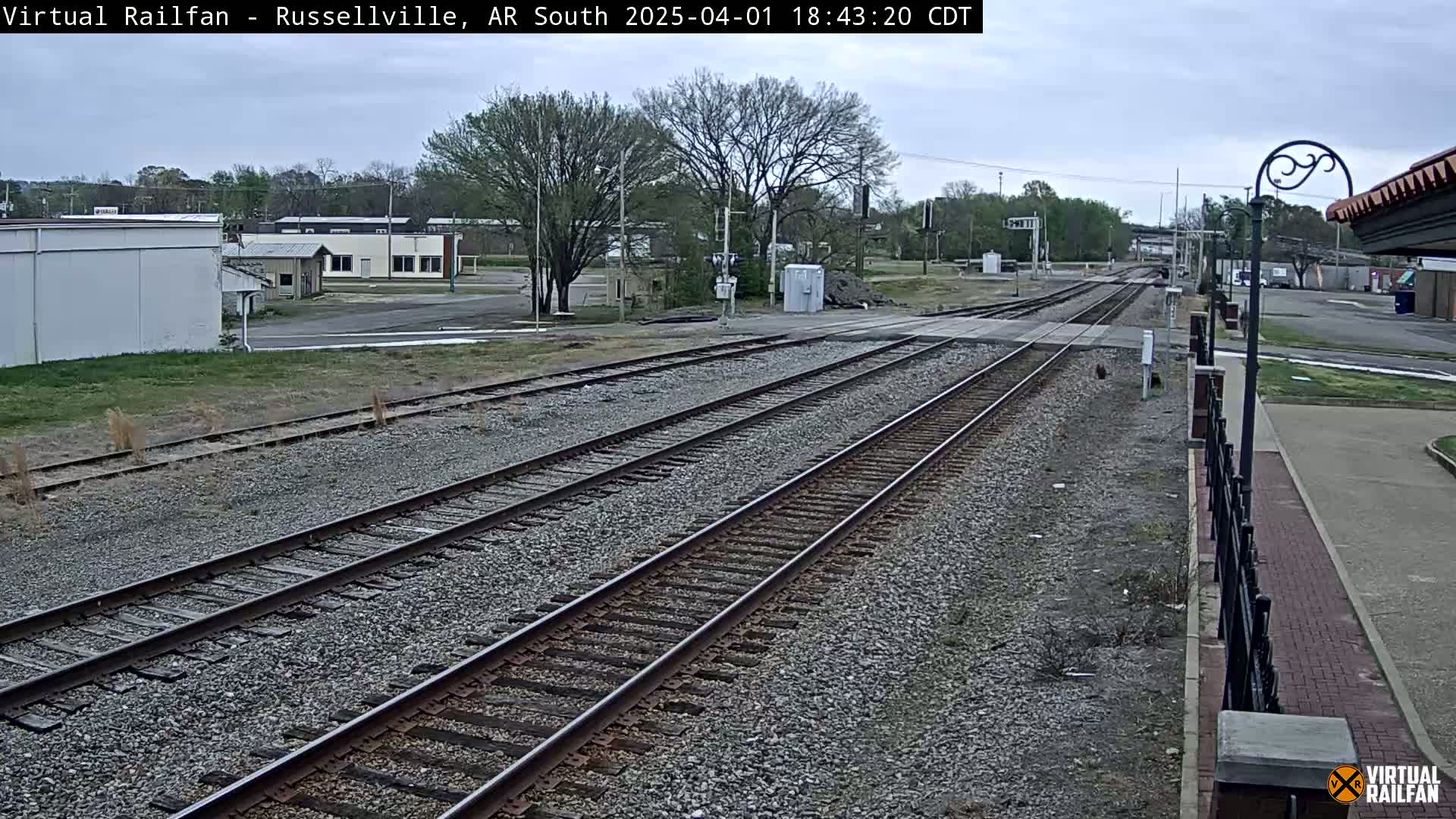 Multiple train tracks extend into the distance under an overcast sky, past a small town with buildings and trees.
