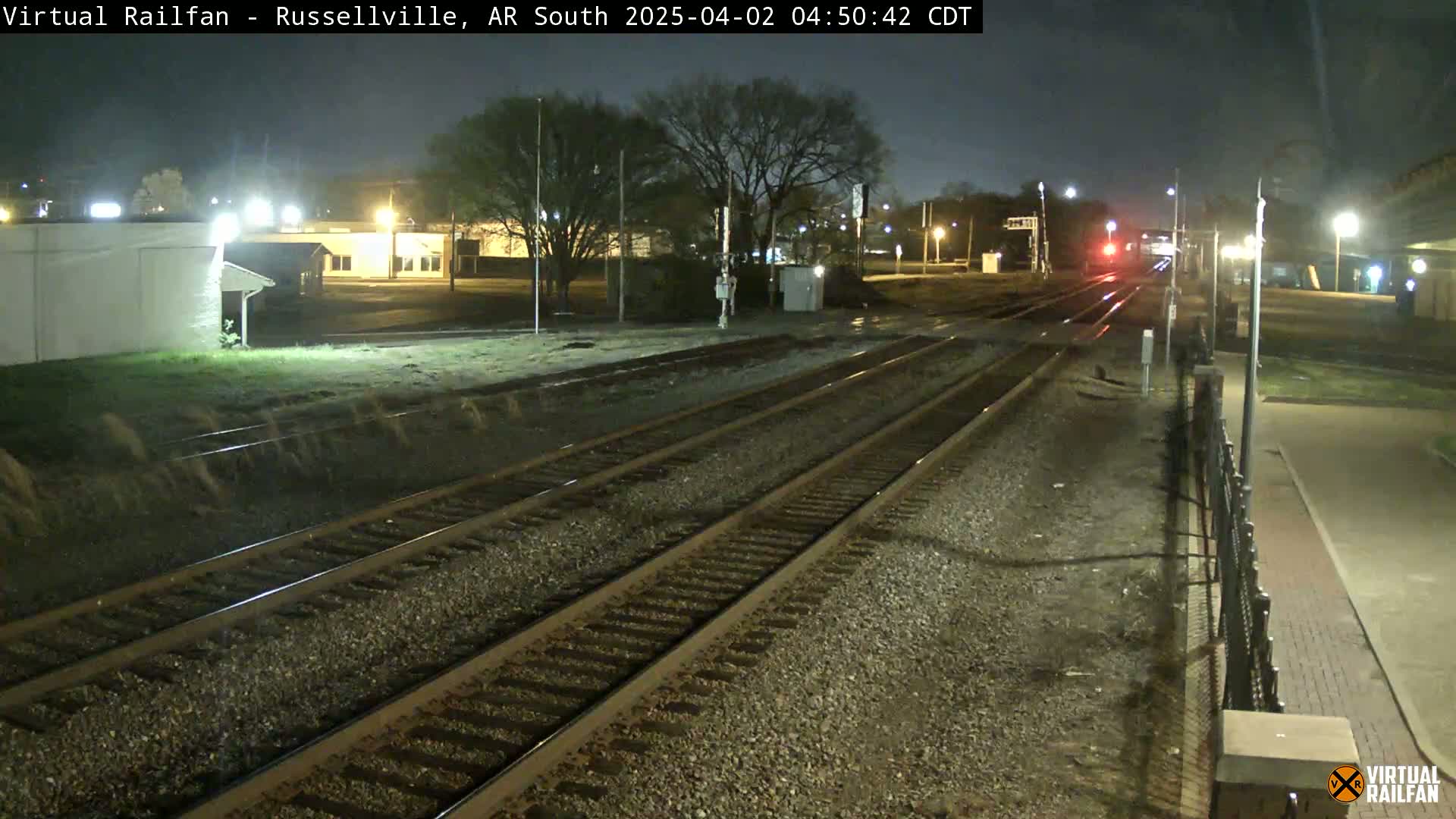 A nighttime view of train tracks at a station, with a train in the distance under dark, clear skies.