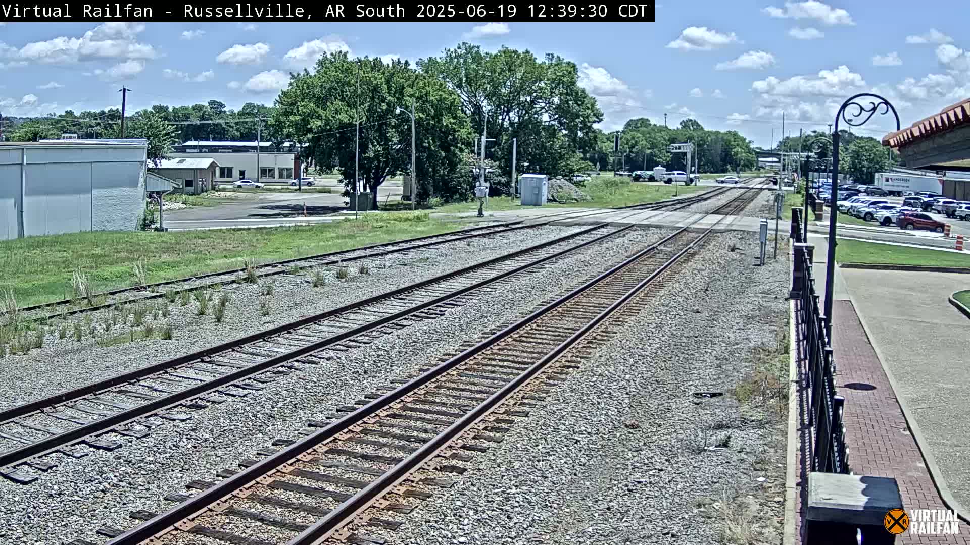 Multiple sets of train tracks stretch toward a town under a partly cloudy sky.