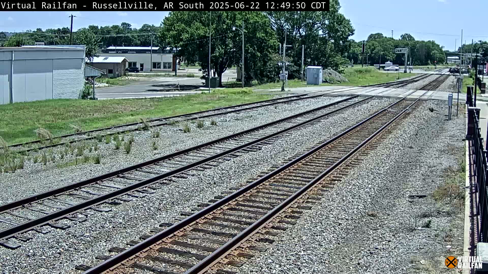 A sunny view of a railroad crossing near some buildings and trees.