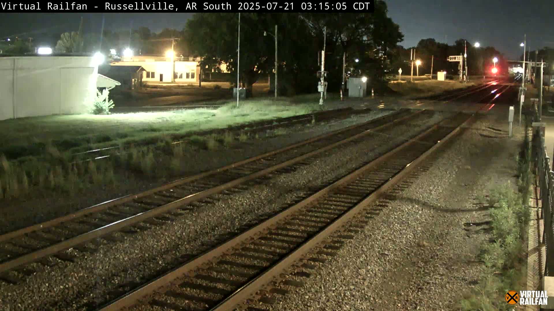 A nighttime view of train tracks and a nearby building under dark, clear skies.
