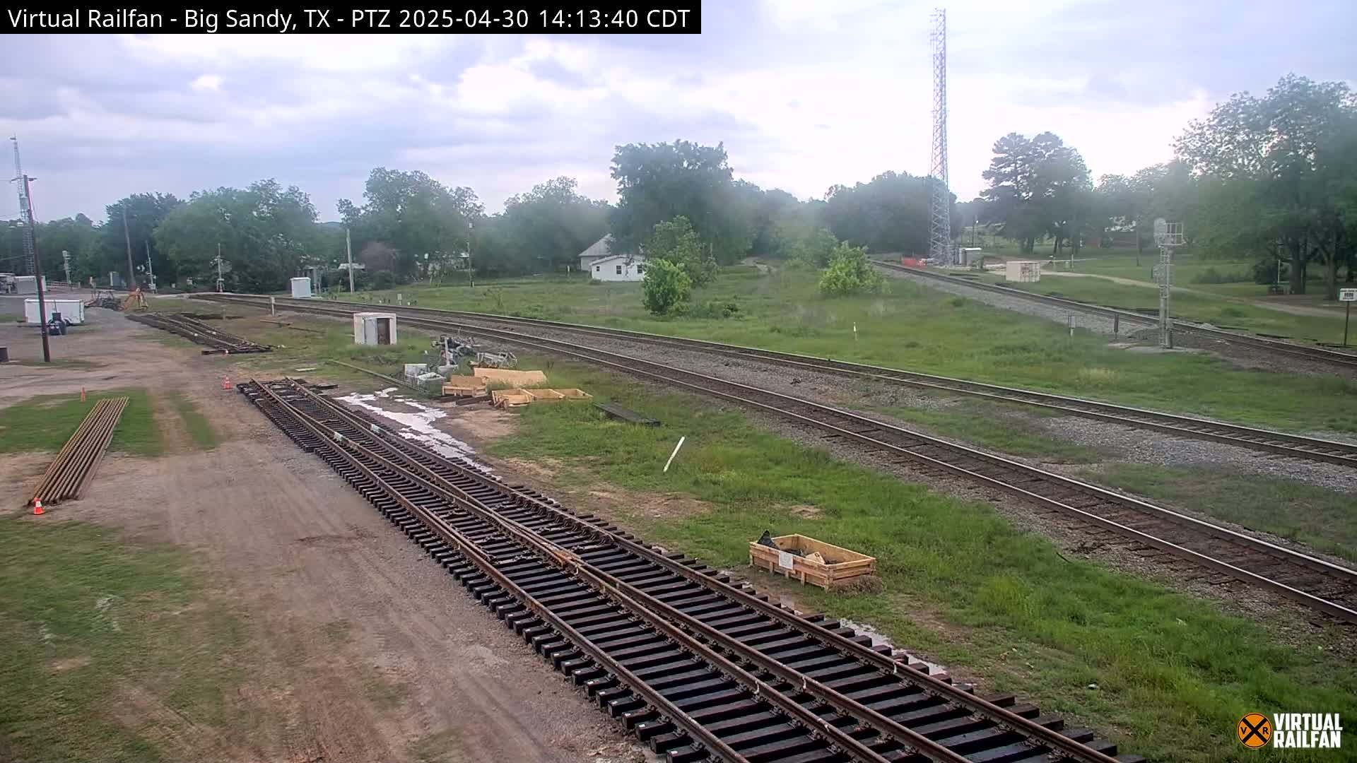 A view of railroad tracks under a partly cloudy sky, with construction materials and equipment visible near the tracks.