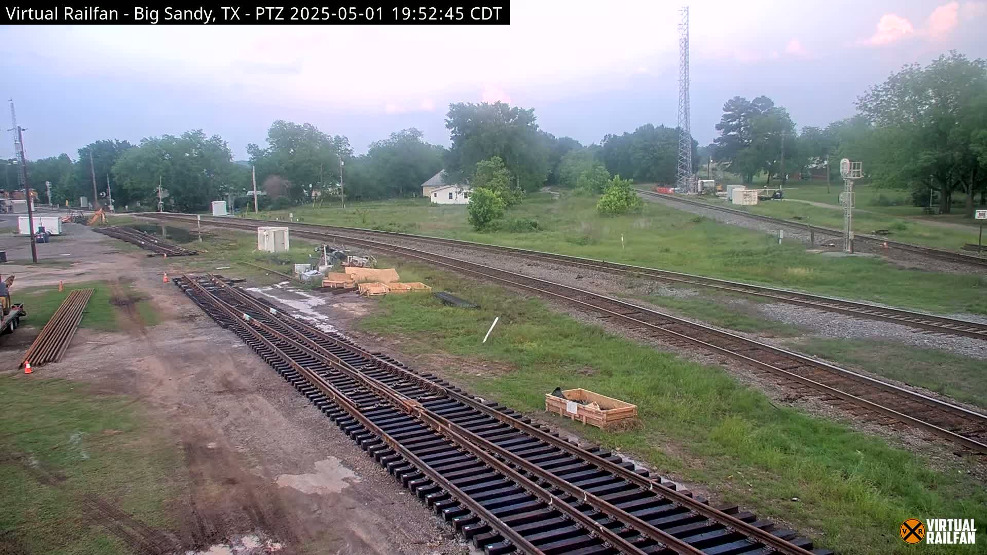 Railroad tracks under construction, surrounded by grassy fields and trees, under an overcast sky.