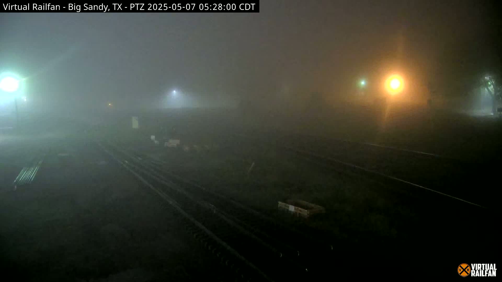 A foggy nighttime scene shows several sets of train tracks illuminated by distant lights.