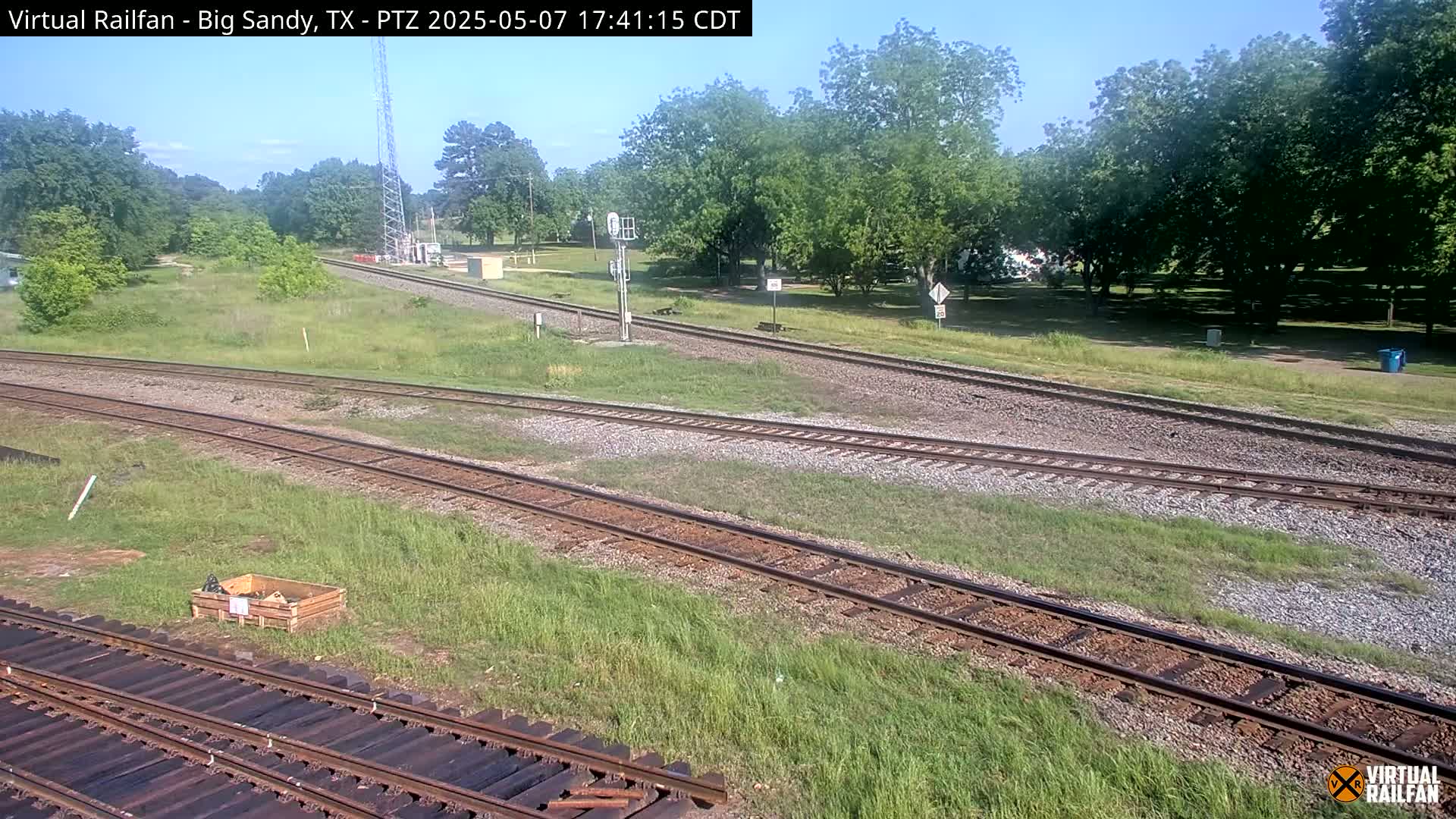 A high-angle view of a train track intersection on a sunny day, surrounded by green grass and trees.