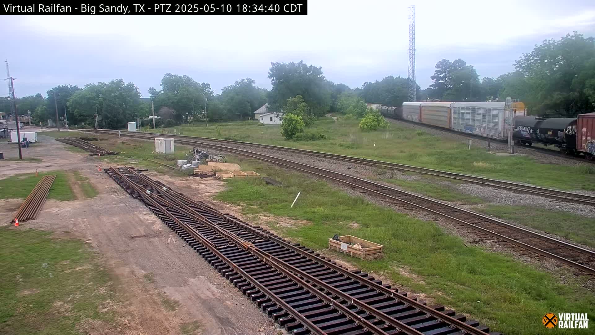 Railroad tracks under construction are visible next to a train passing by in an overcast outdoor setting.