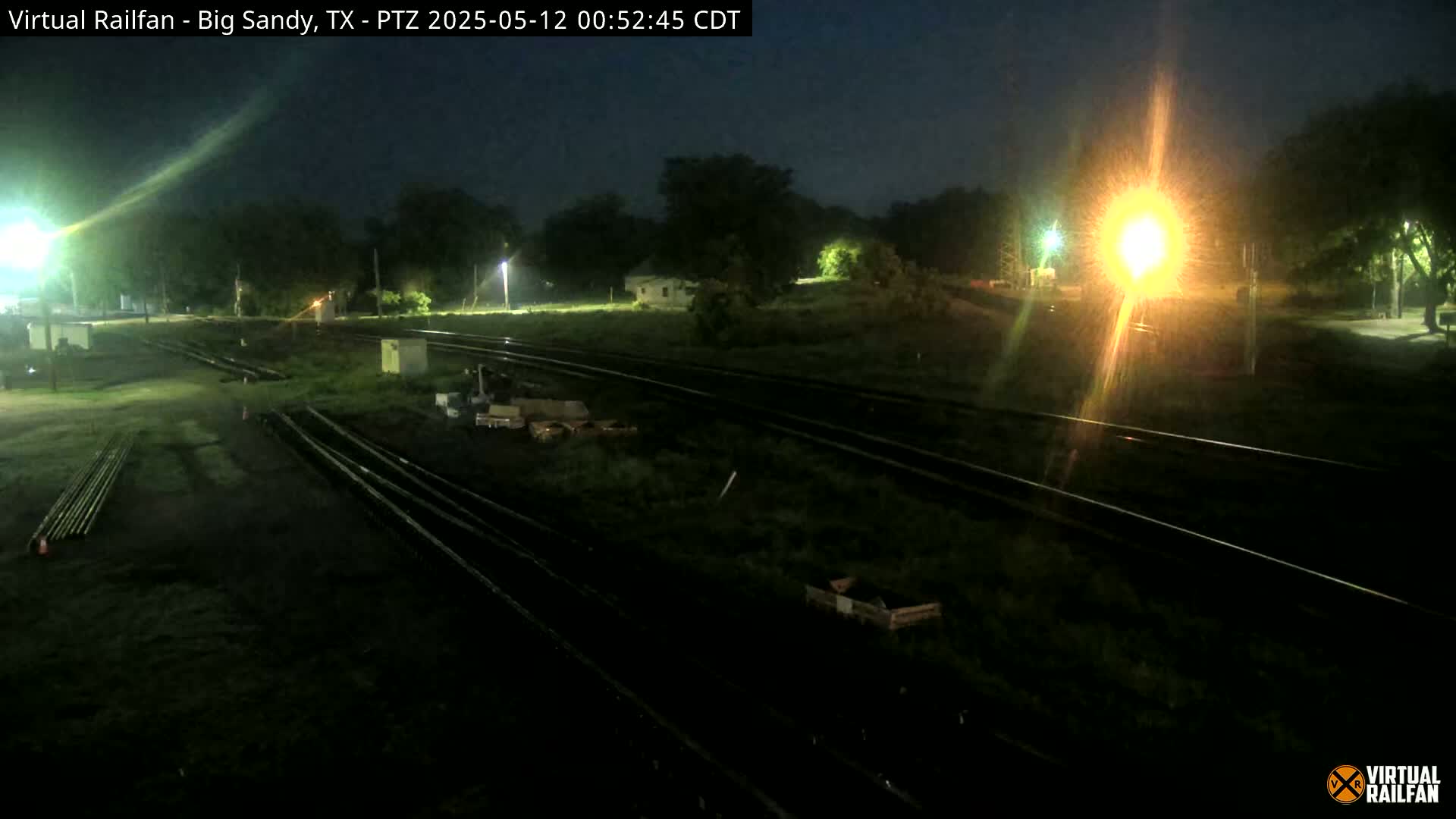 A nighttime view of railroad tracks and surrounding vegetation, lit by artificial lights.