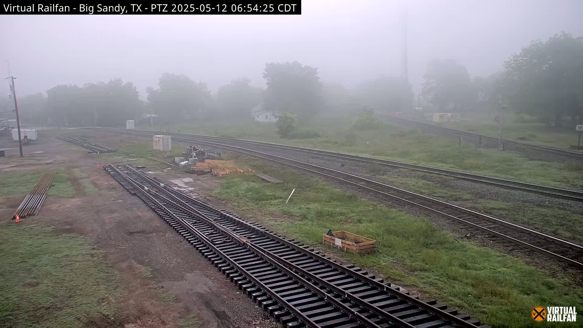 Several sets of train tracks are visible in a foggy, outdoor setting, with some construction materials and equipment nearby.