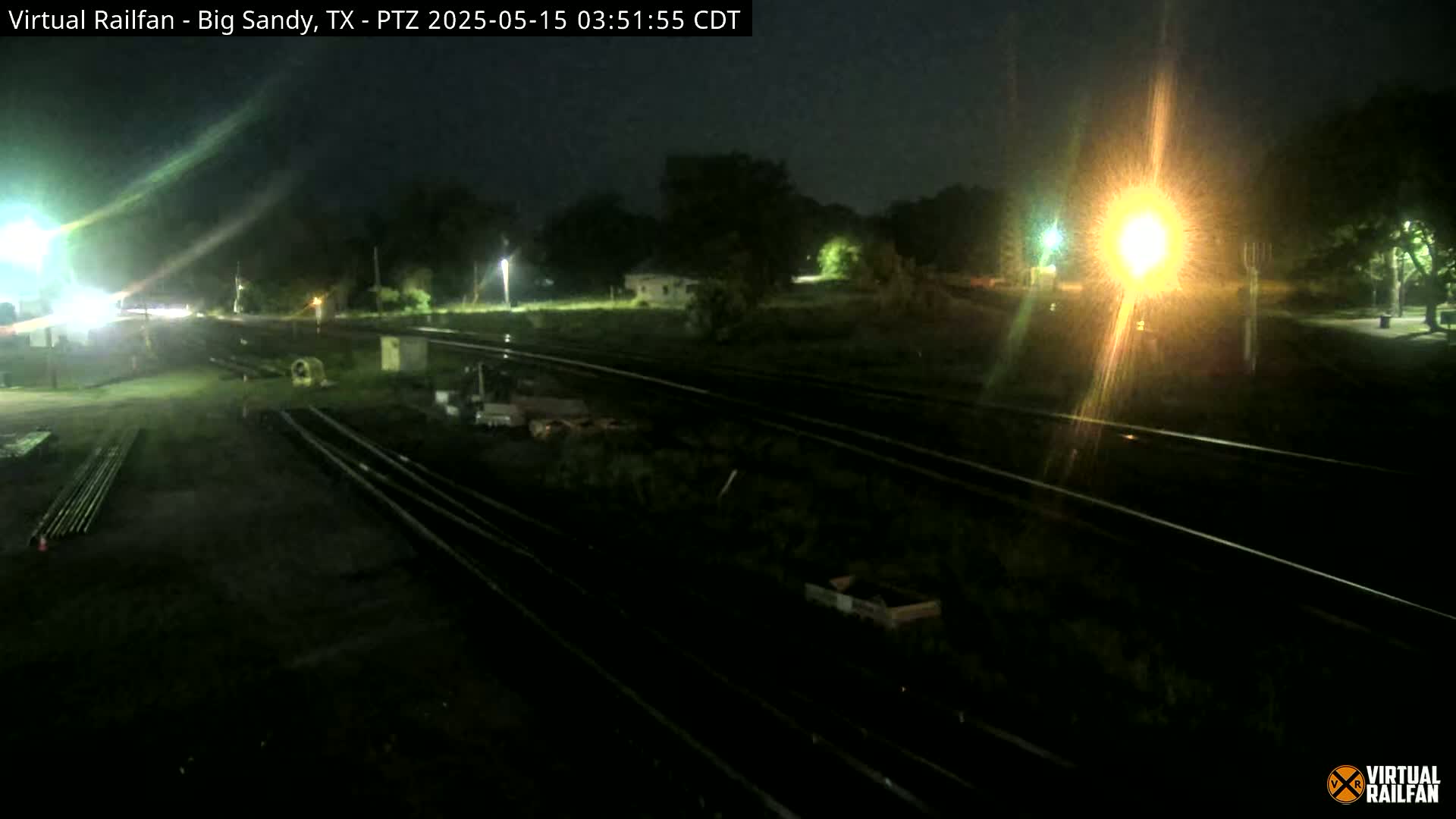 A nighttime view of railroad tracks and surrounding land, illuminated by artificial lights.