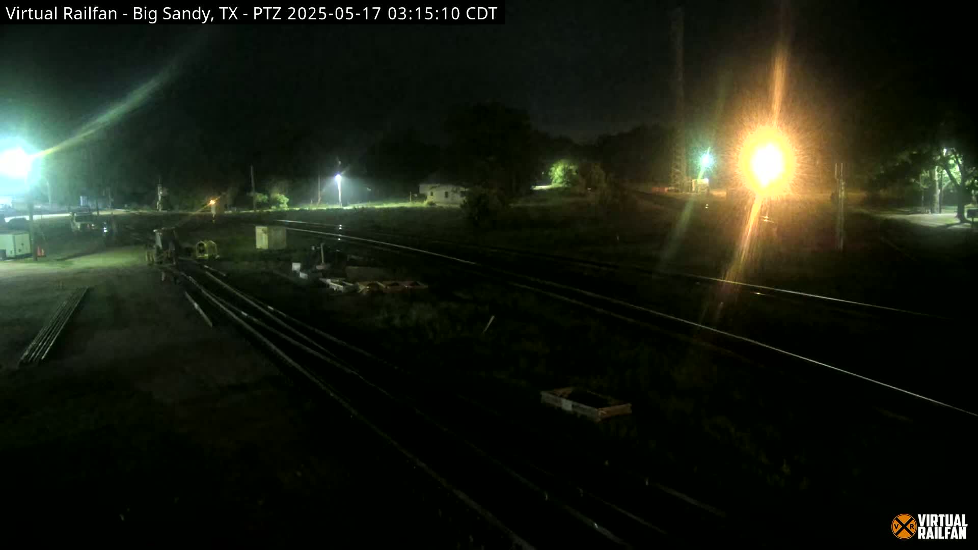 At night, several sets of train tracks are visible, with some equipment and structures nearby under artificial light.