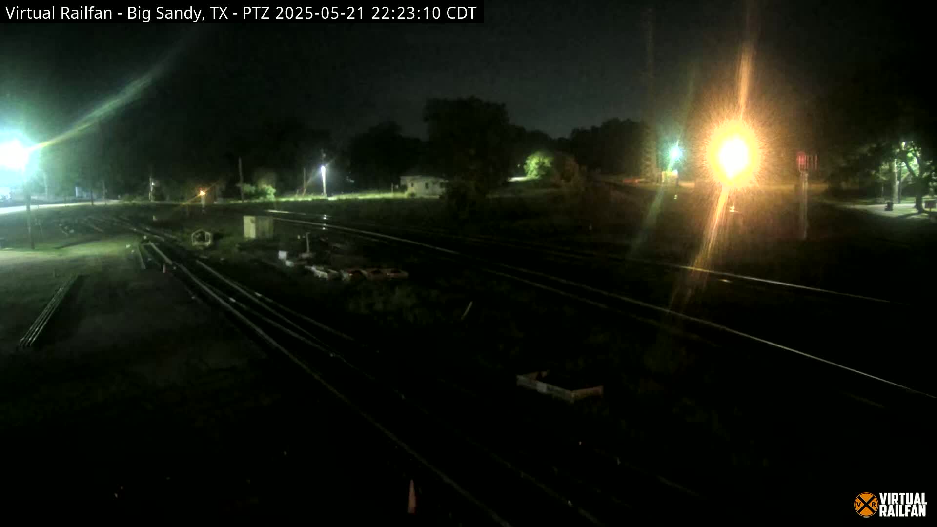 A nighttime view of railroad tracks and surrounding land, illuminated by artificial lights.