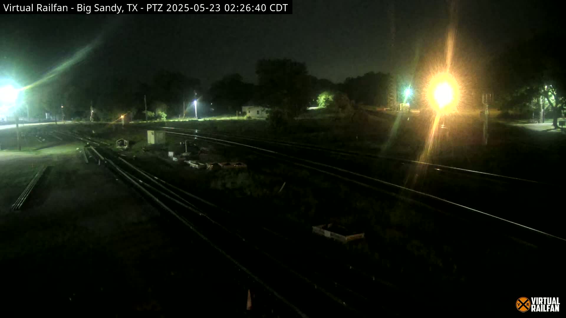 A nighttime view of railroad tracks and surrounding land, illuminated by artificial lights.
