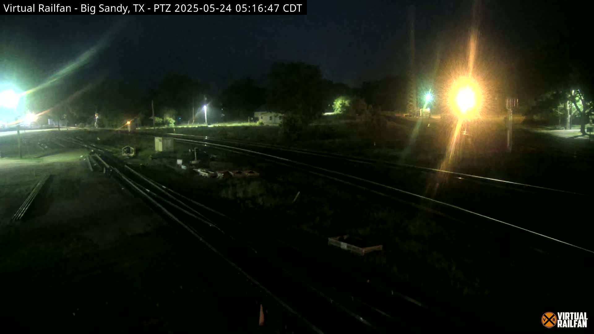 A nighttime view of railroad tracks and surrounding grounds, illuminated by artificial lights.