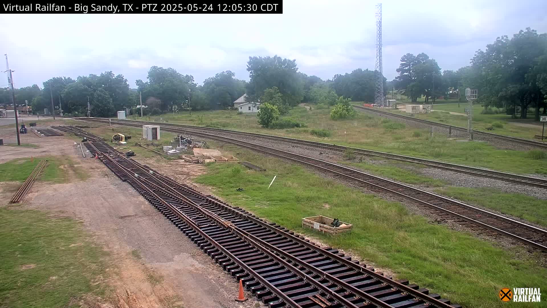 Railroad tracks under construction are situated in a grassy area next to a small town under an overcast sky.