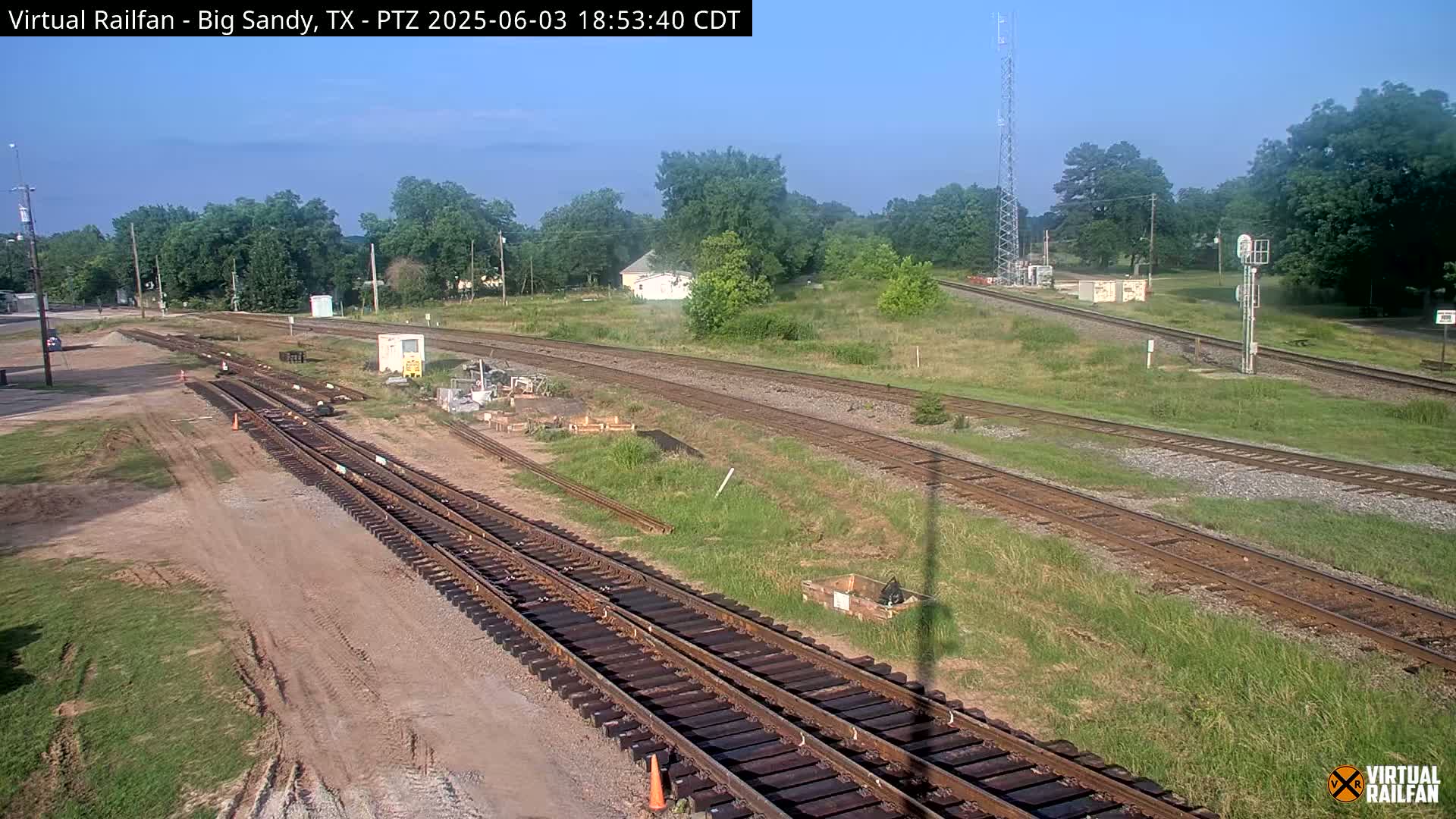 Several sets of train tracks intersect in a grassy area, under a clear sky.