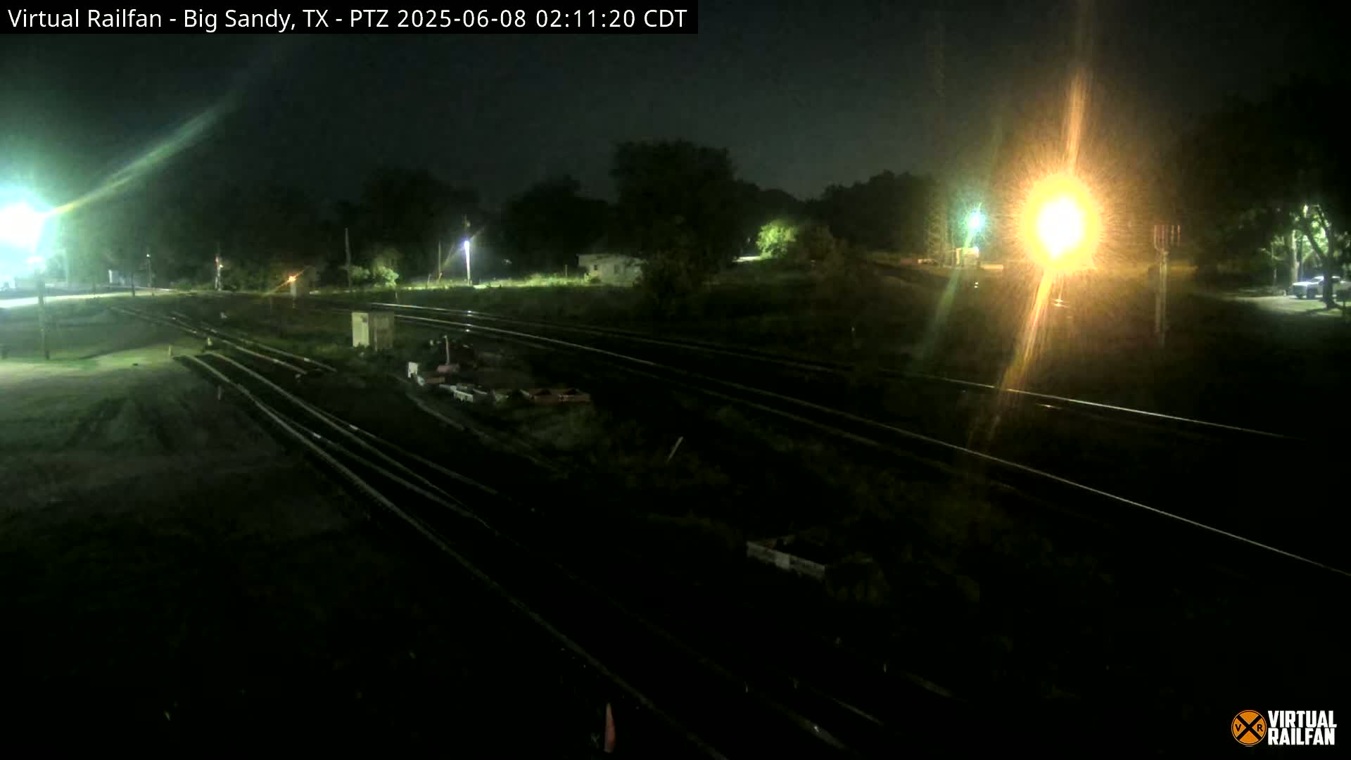 A nighttime view of train tracks and surrounding land, illuminated by artificial lights.