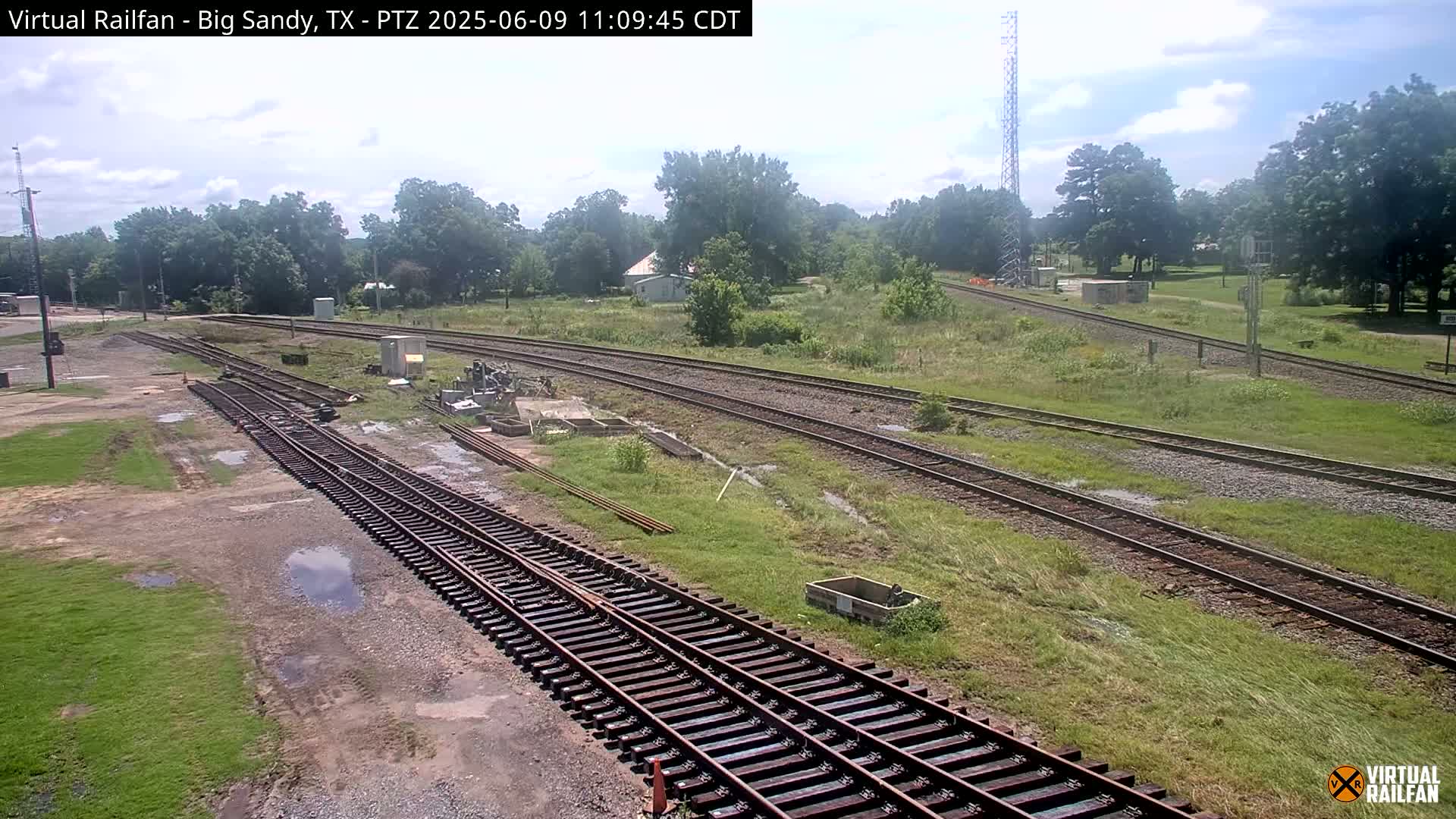 Several sets of railroad tracks wind through a grassy area under a partly cloudy sky.