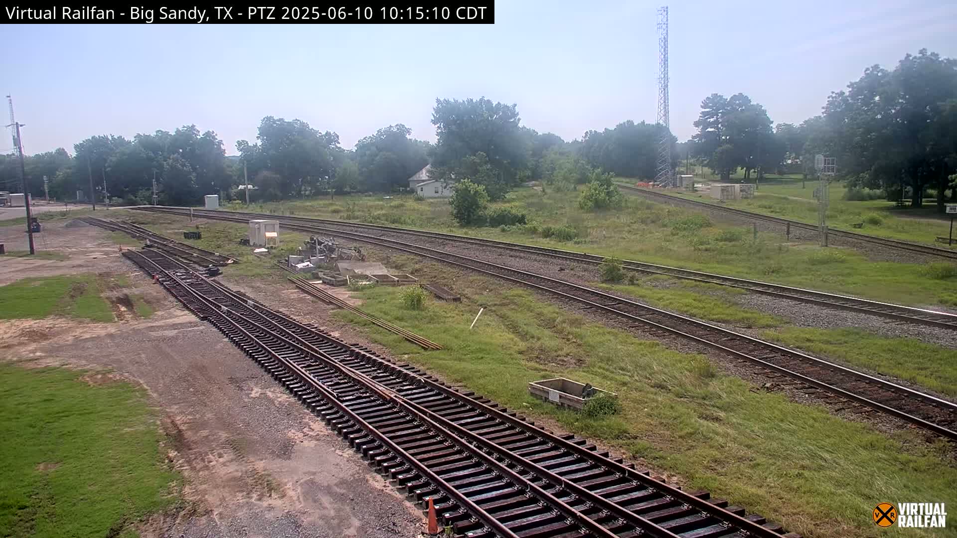 A high-angle, long shot shows several sets of train tracks curving through a grassy area under a mostly clear sky.