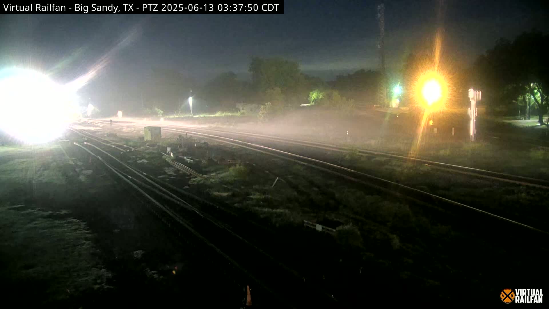 Multiple train tracks at night are partially obscured by fog or mist under bright artificial lights.