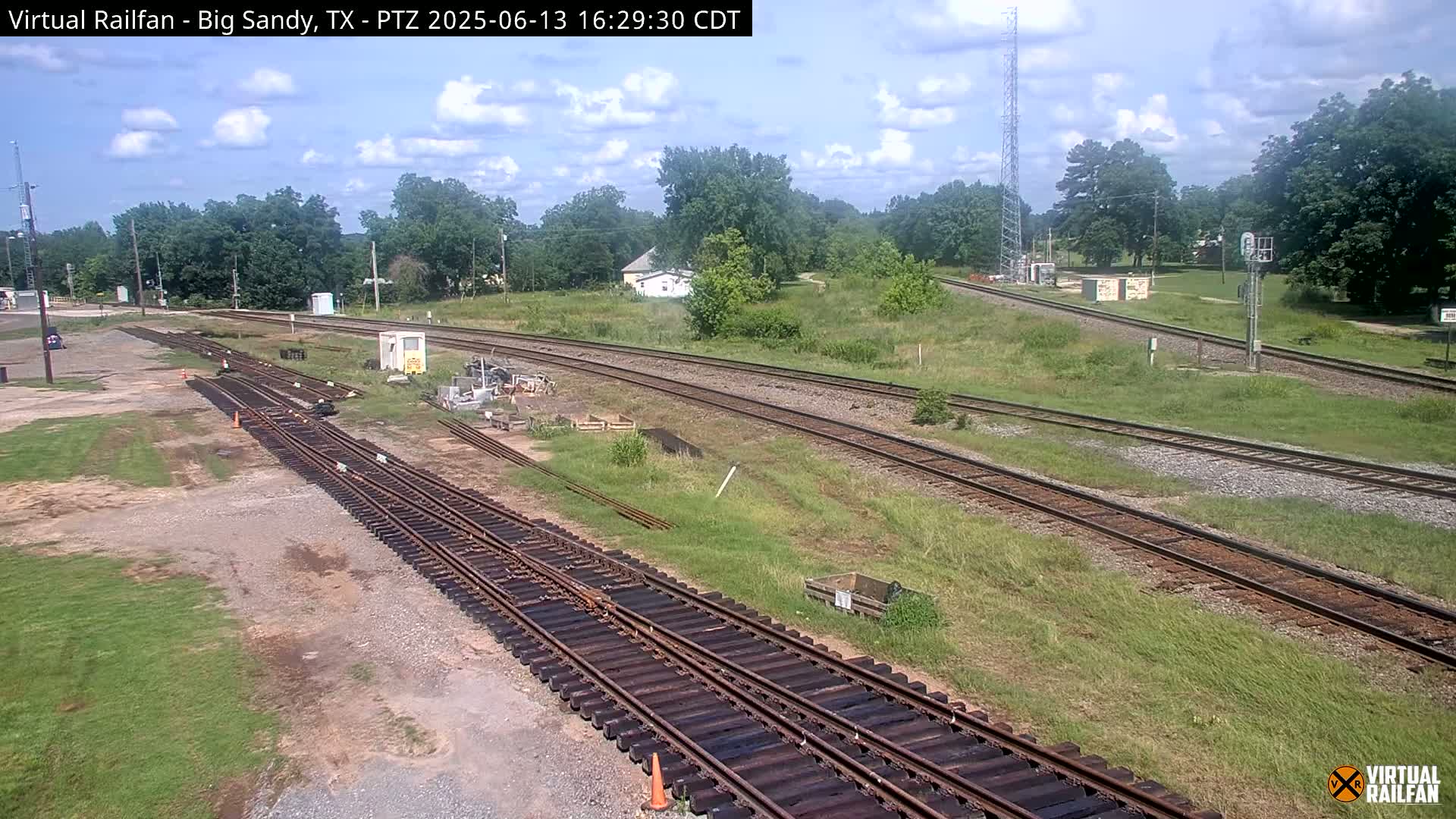 Several sets of railroad tracks curve through a grassy area under a partly cloudy sky.