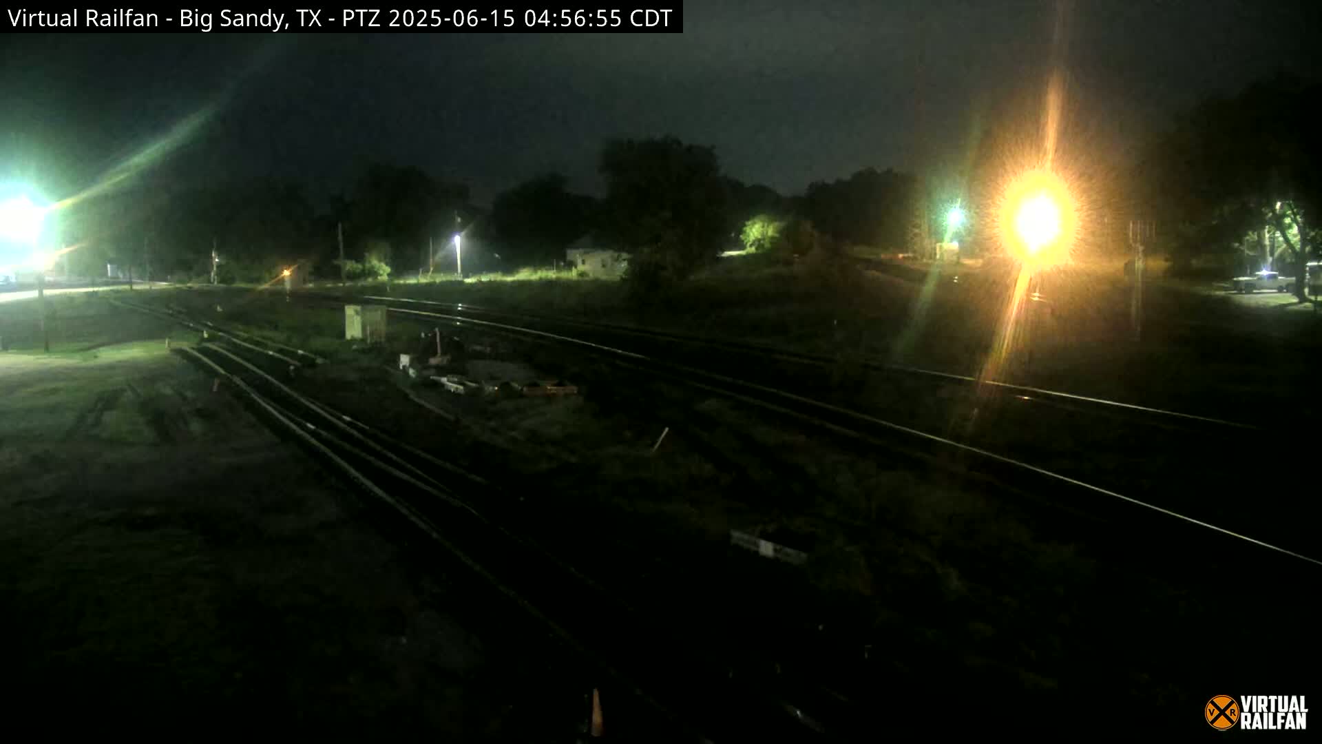At night, a nighttime view shows a railroad yard with train tracks extending into the darkness, illuminated by artificial lights.