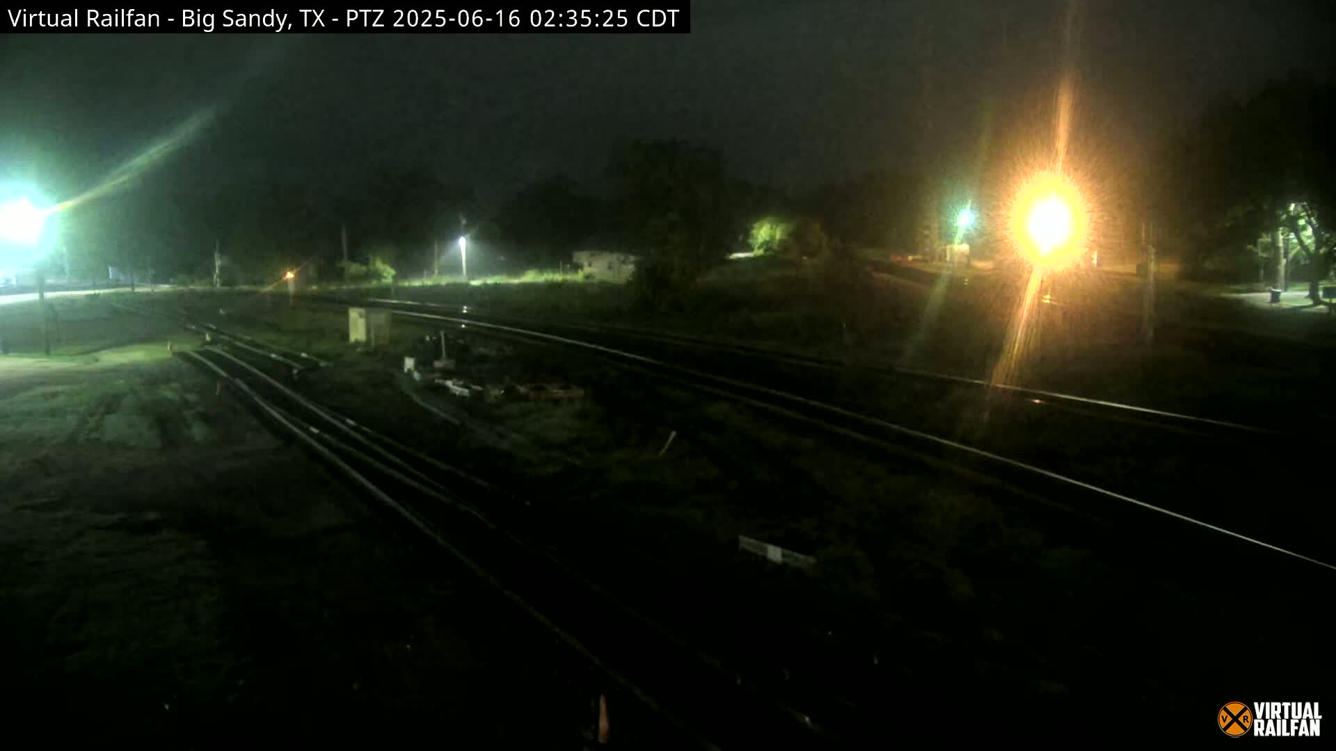 A nighttime view of railroad tracks under rainy conditions, illuminated by streetlights.