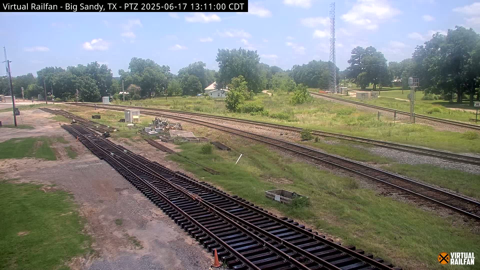 Several sets of train tracks curve through a grassy area under a partly sunny sky.