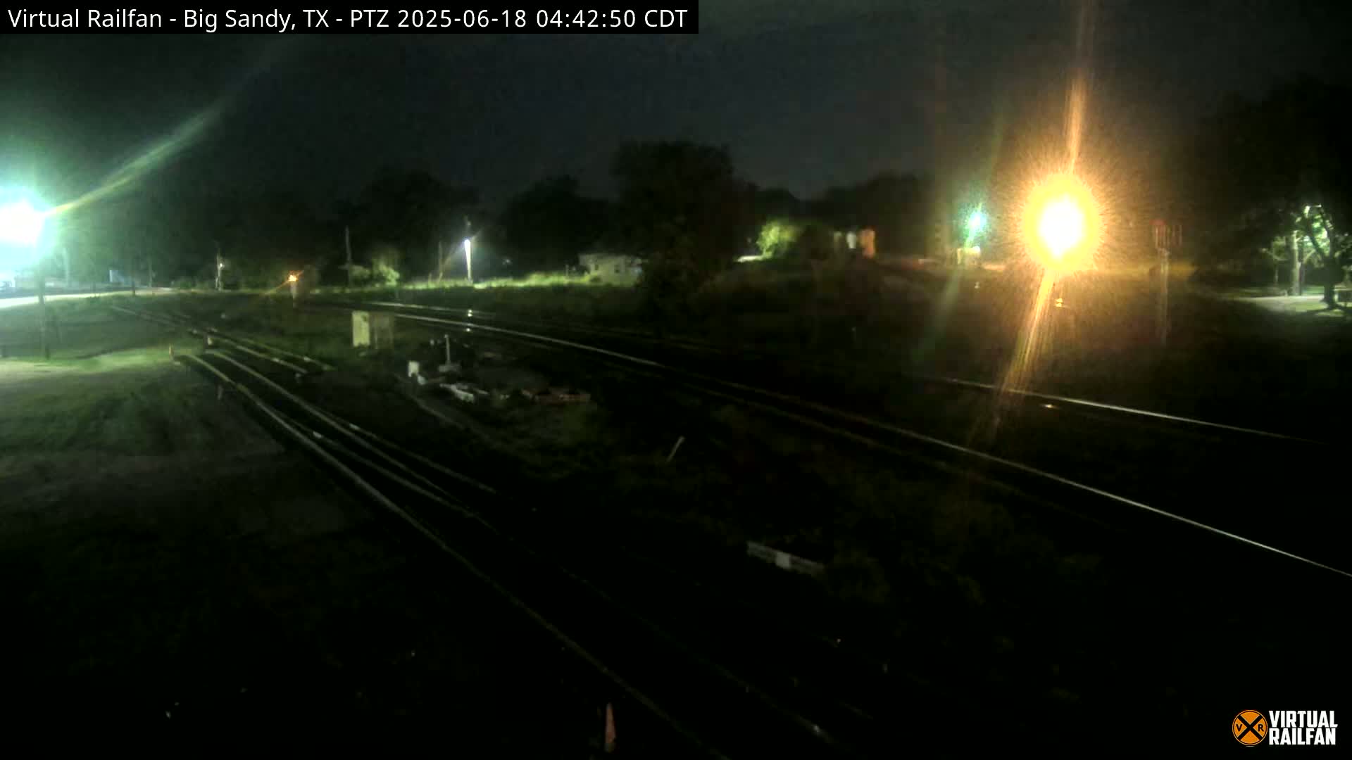 A nighttime view of railroad tracks and surrounding vegetation under a dark sky.