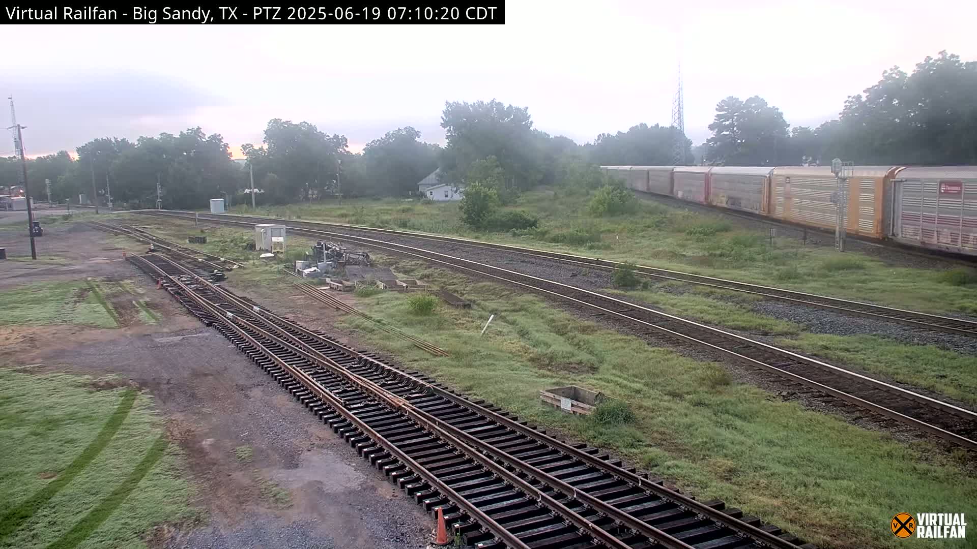 A long freight train sits on tracks next to a railway switching yard on a foggy morning.